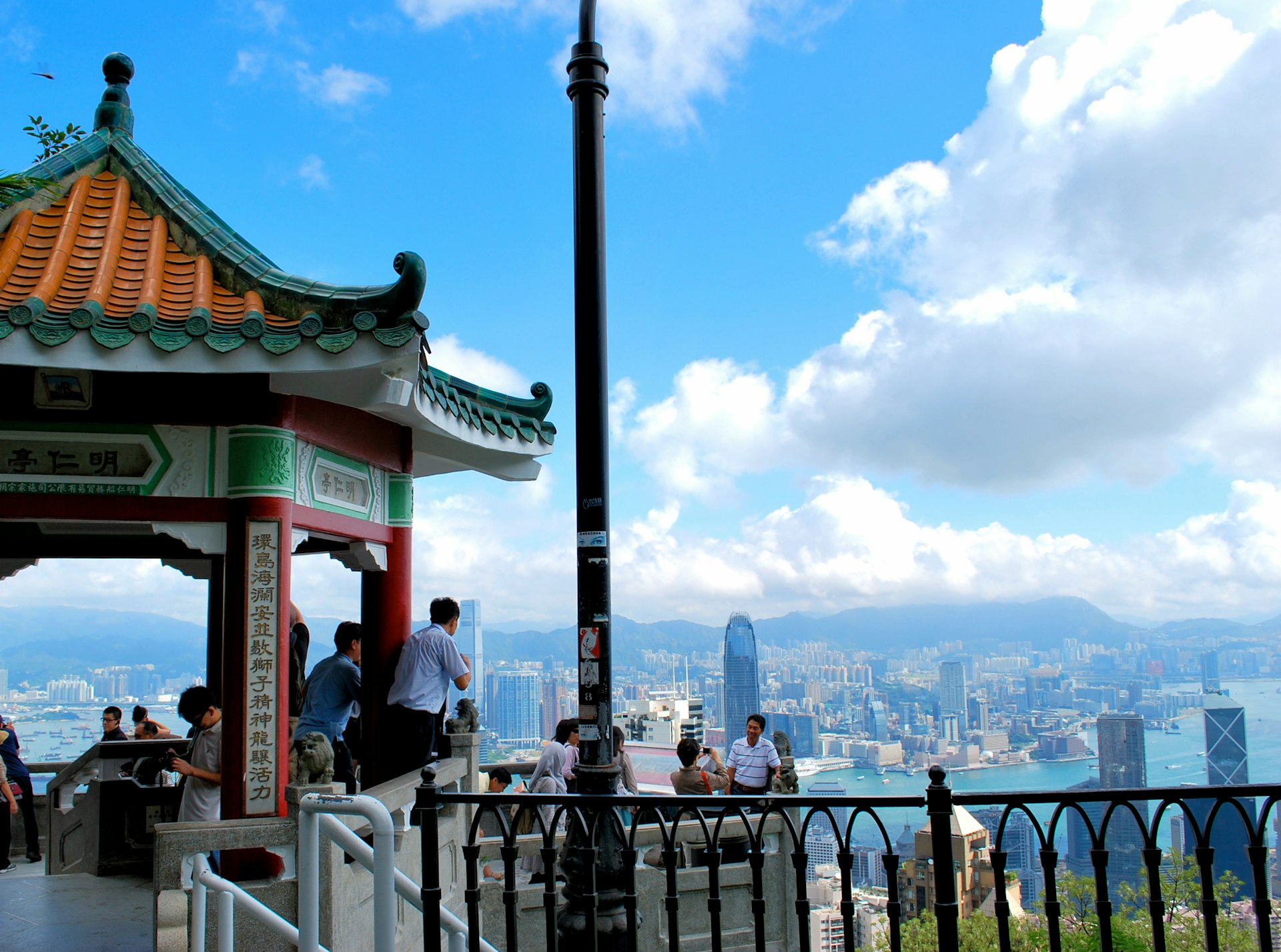 People pose for photos at the viewpoint of Victoria Peak, with high-rise Hong Kong buildings behind them