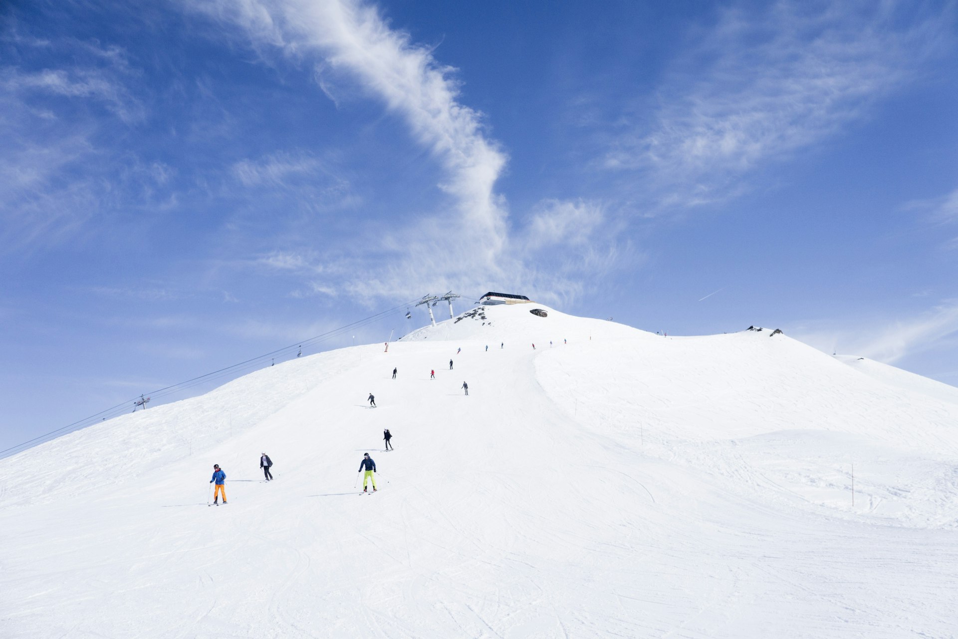View from bottom of a ski hill of a bunch of skiers making their way down the hill, with a chair lift in the background
