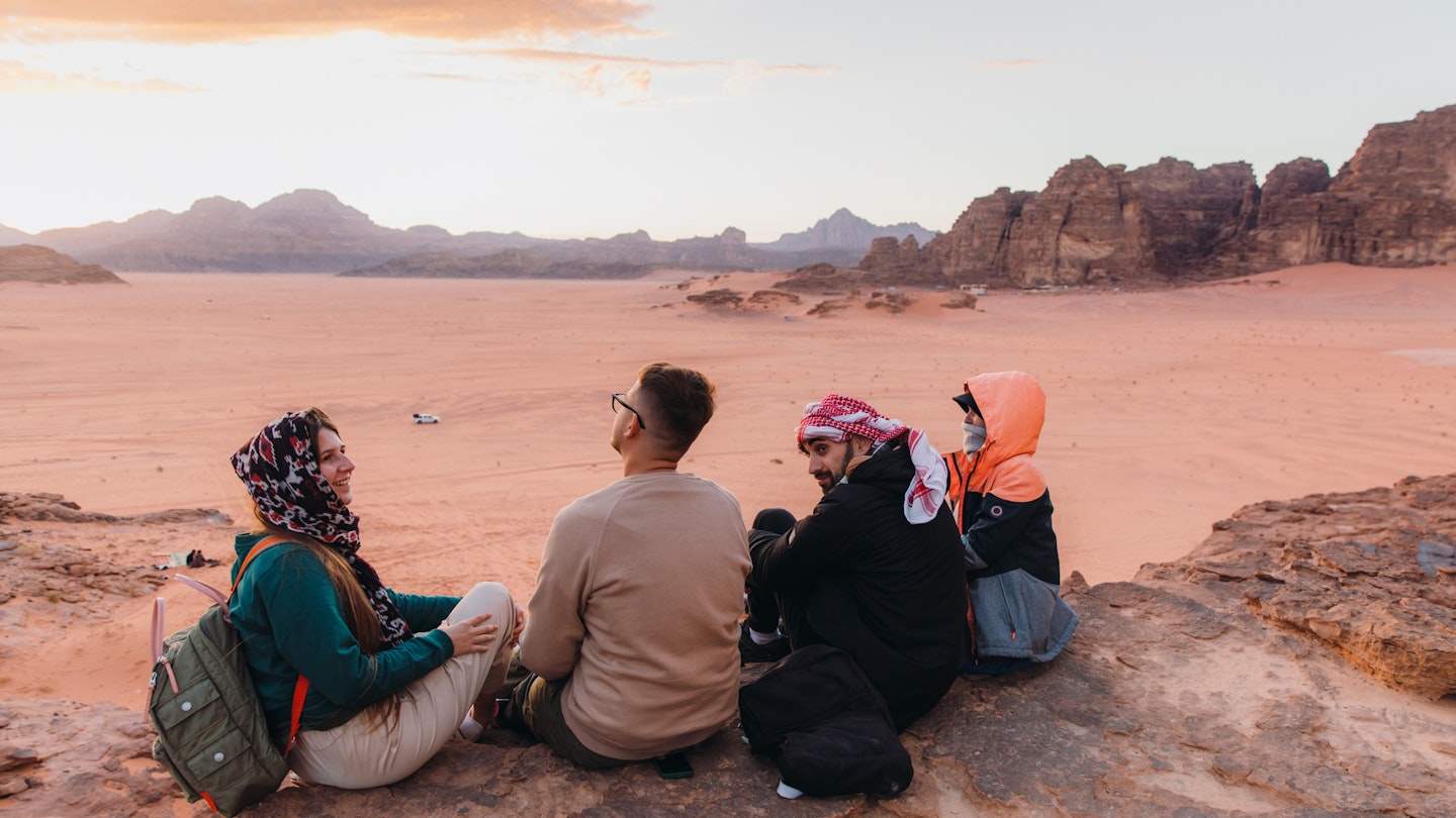 Mixed-race group of females and males having picnic at the edge of the cliff with view of the red sands and majestic mountains in Wadi Rum, Middle East