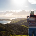 Travel guide, tourism in New Zealand, woman taking a picture in The Coromandel Coastal Walkway; Shutterstock ID 1878838228; your: Sloane Tucker; gl: 65050; netsuite: Online Editorial; full: New Zealand Best Hikes Article