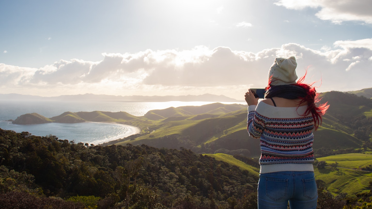 Travel guide, tourism in New Zealand, woman taking a picture in The Coromandel Coastal Walkway; Shutterstock ID 1878838228; your: Sloane Tucker; gl: 65050; netsuite: Online Editorial; full: New Zealand Best Hikes Article