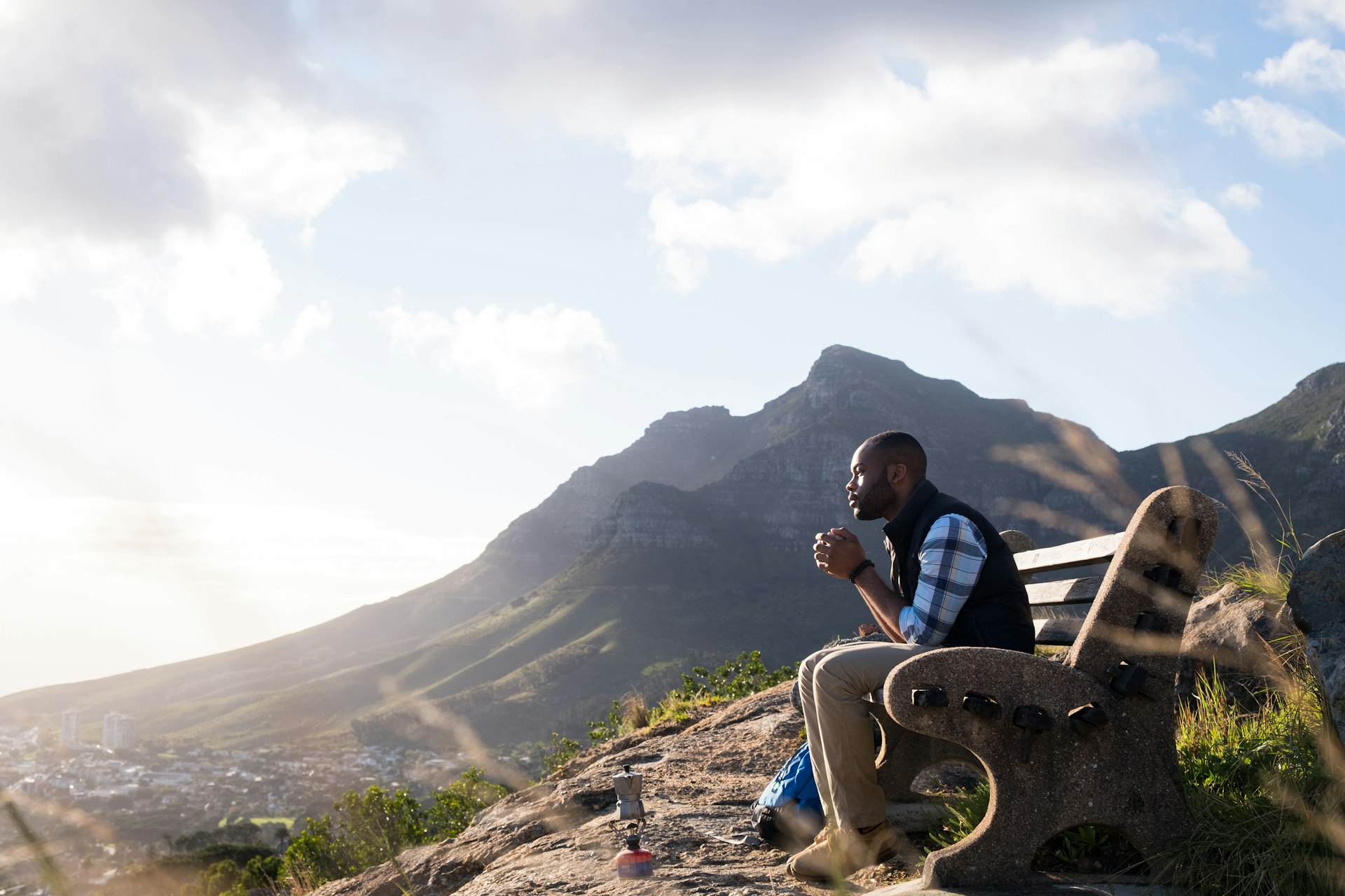 Side view of male hiker sitting on a bench, having a drink and looking at Table Mountain. 