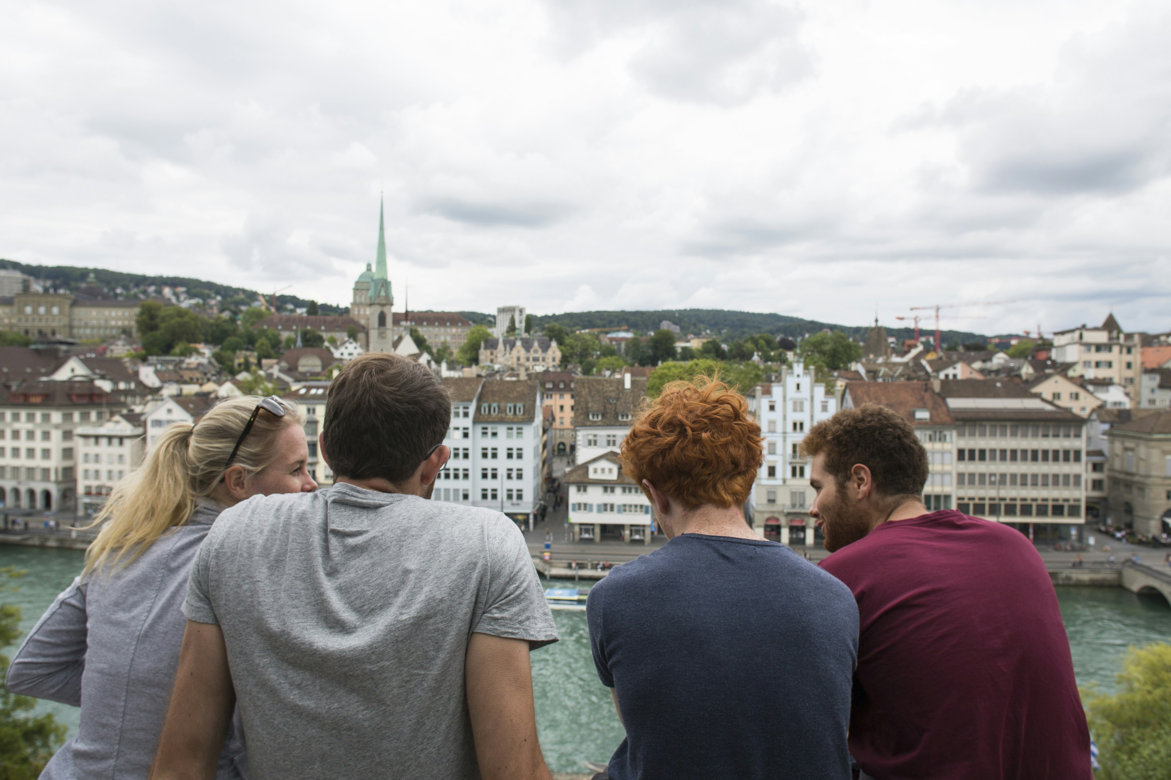A group of 4 young friends, a blonde young woman and three guys, one of them has red hair, looking out on the terrace of the Lindenhof Zurich.