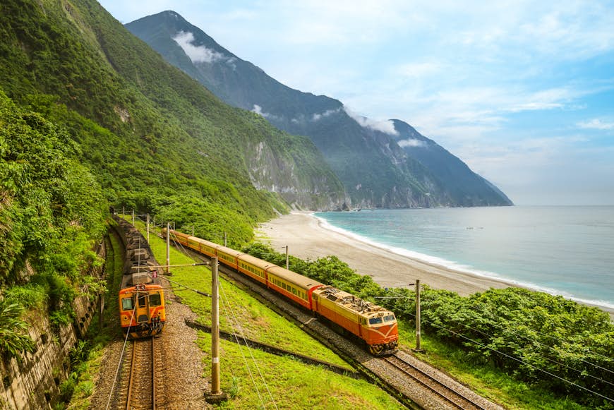 Two trains on a lush green coastline with a tall peak in the distance