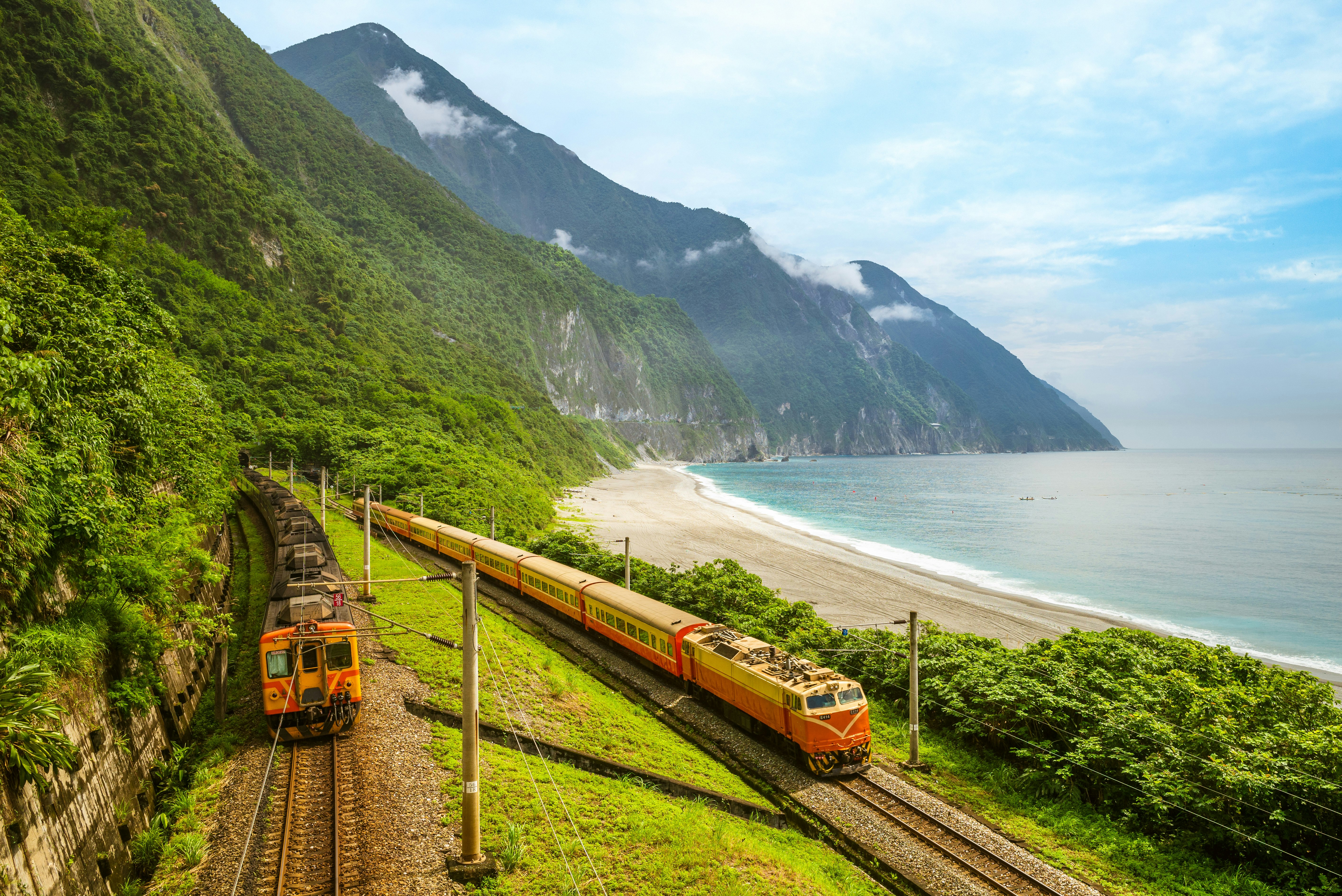 Two trains on a lush green coastline with a tall peak in the distance