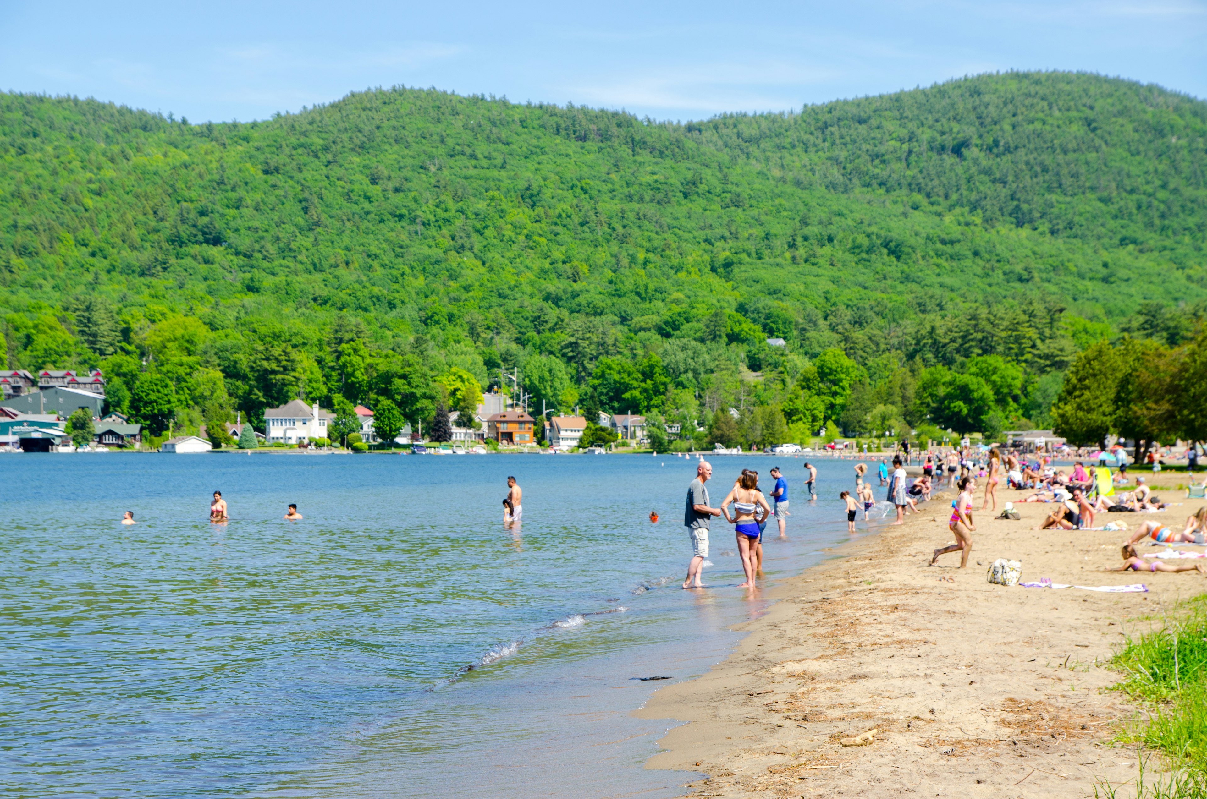 Crowd of swimmers on beach of Lake George (NY) during day of springtime