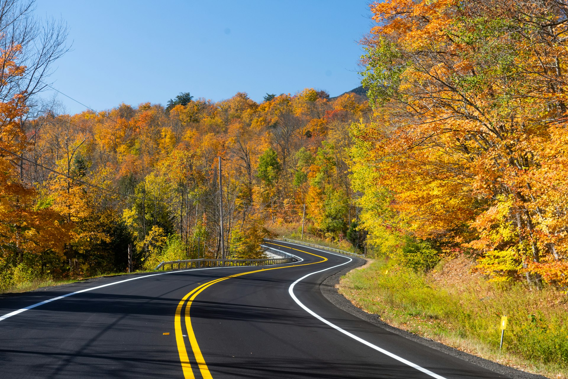 Trees with autumn leaves line a scenic road through the Adirondack Mountains, New York State, USA