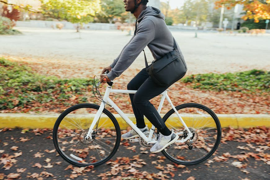 An adult Black man enjoys a bicycle ride on a brisk and sunny autumn day in the Pacific Northwest. The fall leaves glow in the sunlight. Shot in Seattle, Washington, USA.
