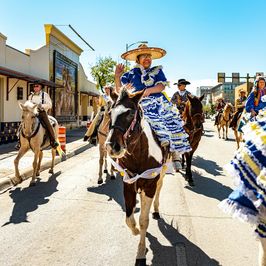 San Antonio, Texas, USA-February 1, 2020. Young Mexican woman riding a horse in Rodeo parade with horses at Historic Market Square in downtown San Antonio. People dressed in traditional wardrobe of old times. Mexican culture, Pioneer explorers culture. Horse riding on downtown city streets.