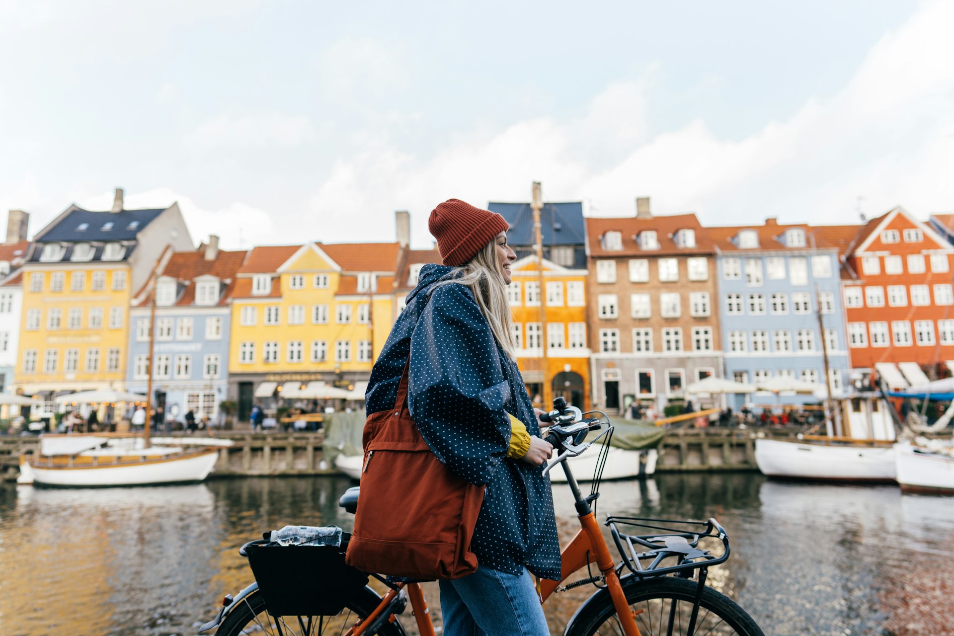 Photo of a young woman pulling the bike and walking down the street while exploring the famous tourist attraction in Copenhagen, Denmark