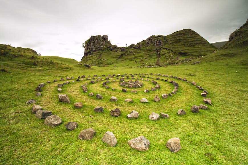 A mystical-looking stone circle its in the lush green grass of Scotland. 