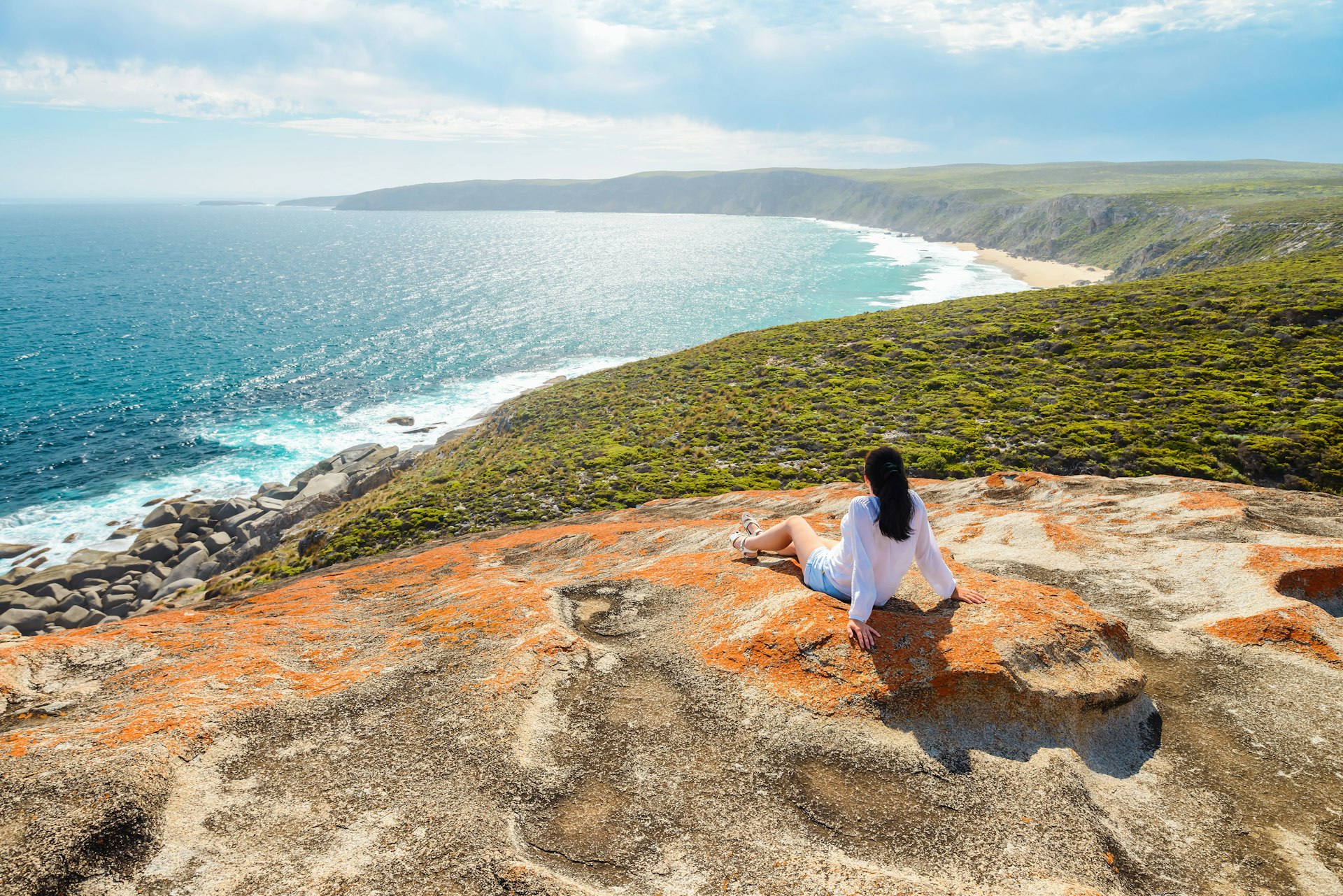 Woman enjoying the scenery while sitting on the edge of the cliff at Remarkable Rocks, Kangaroo Island, South Australia.