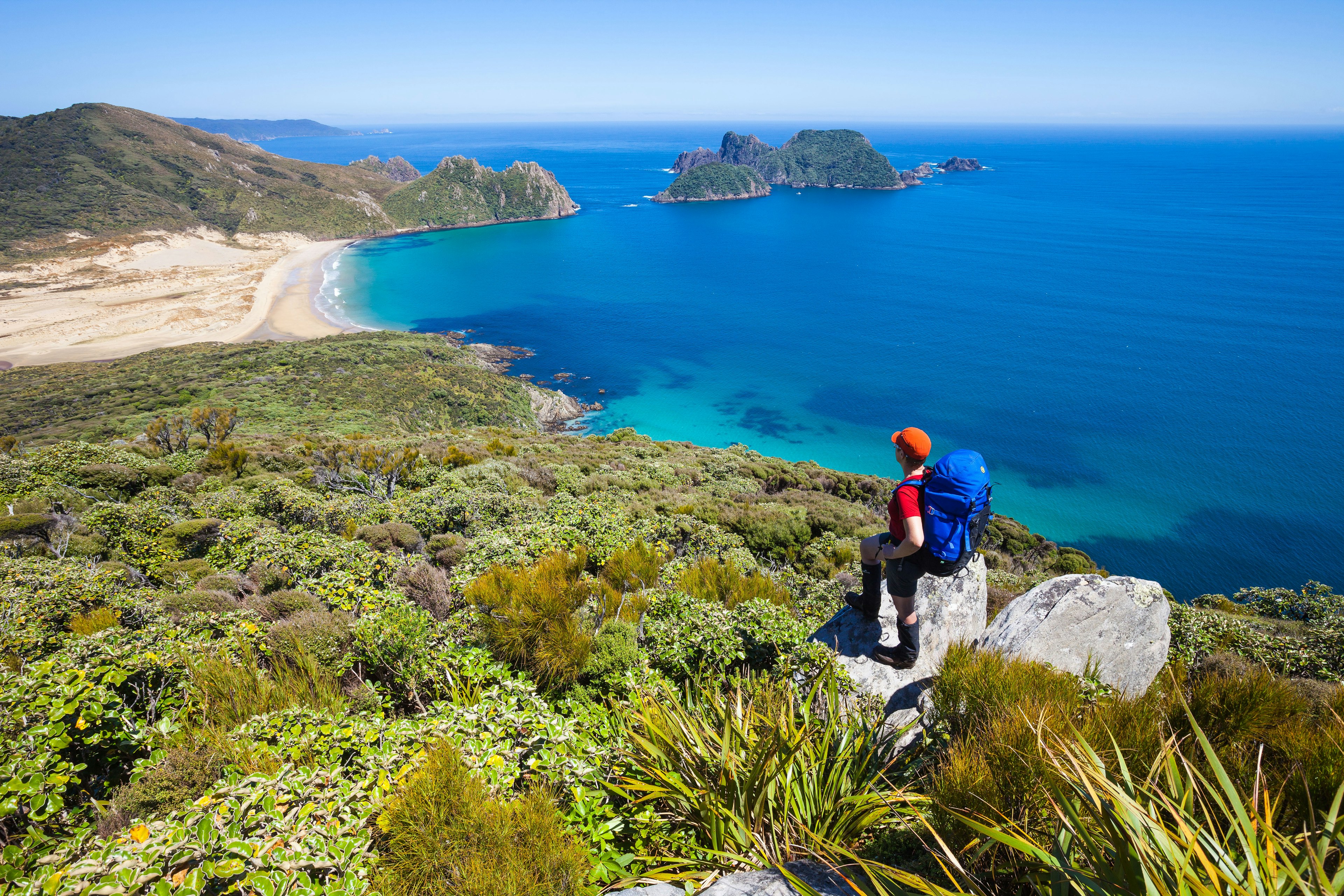 A woman hiker stands on a high ledge overlooking the coastline.