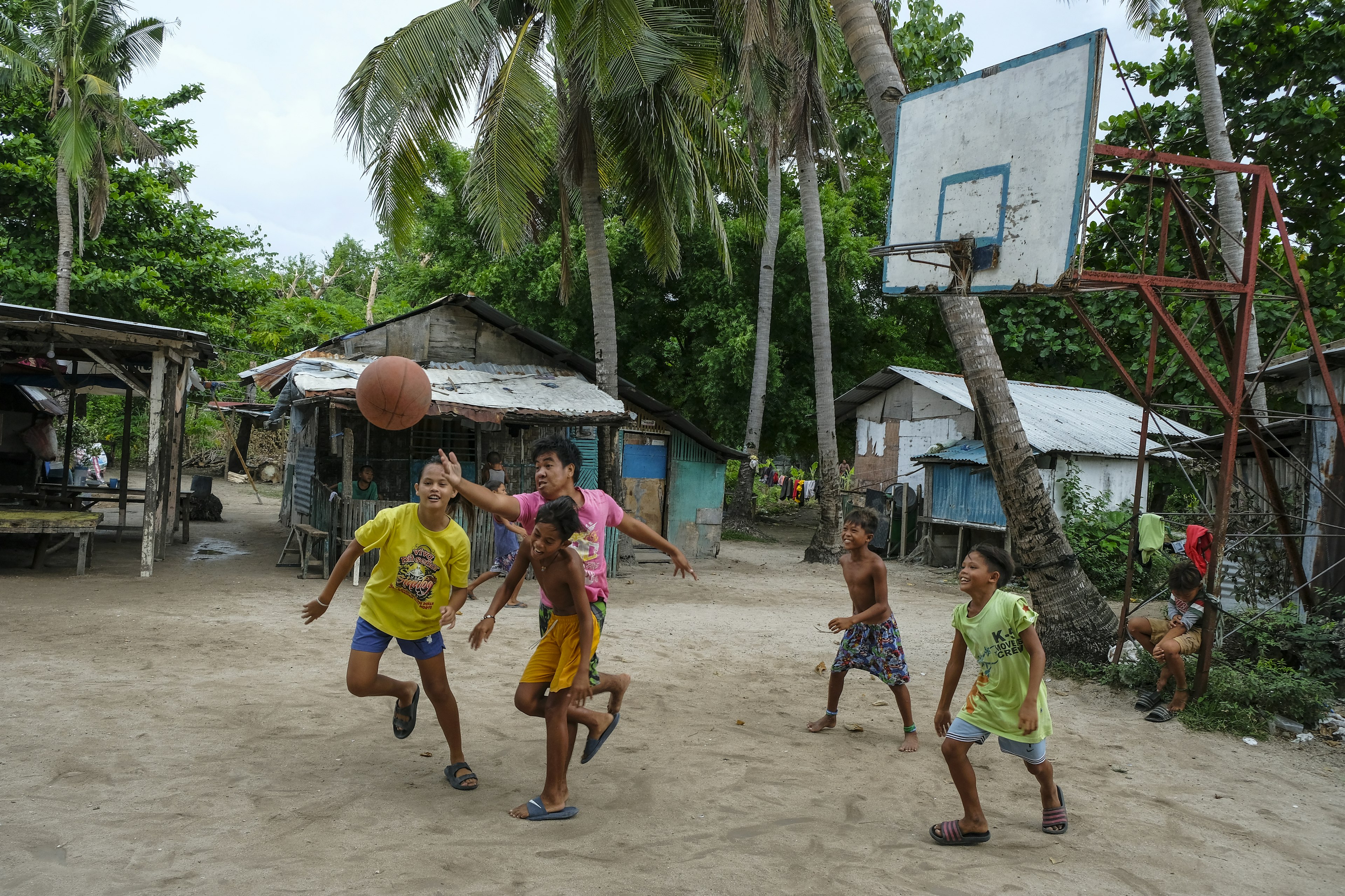 Children playing basketball in front of wooden homes in the Philippines.