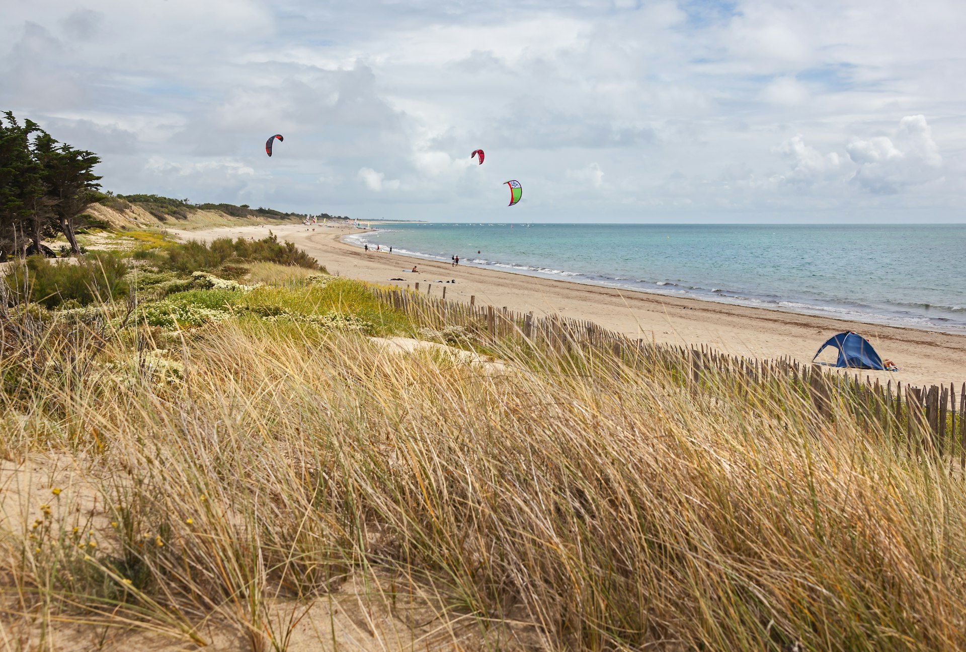 Kite surfing on the deserted Atlantic beach on the island of Ile de Re with dunes covered with grass in the foreground.