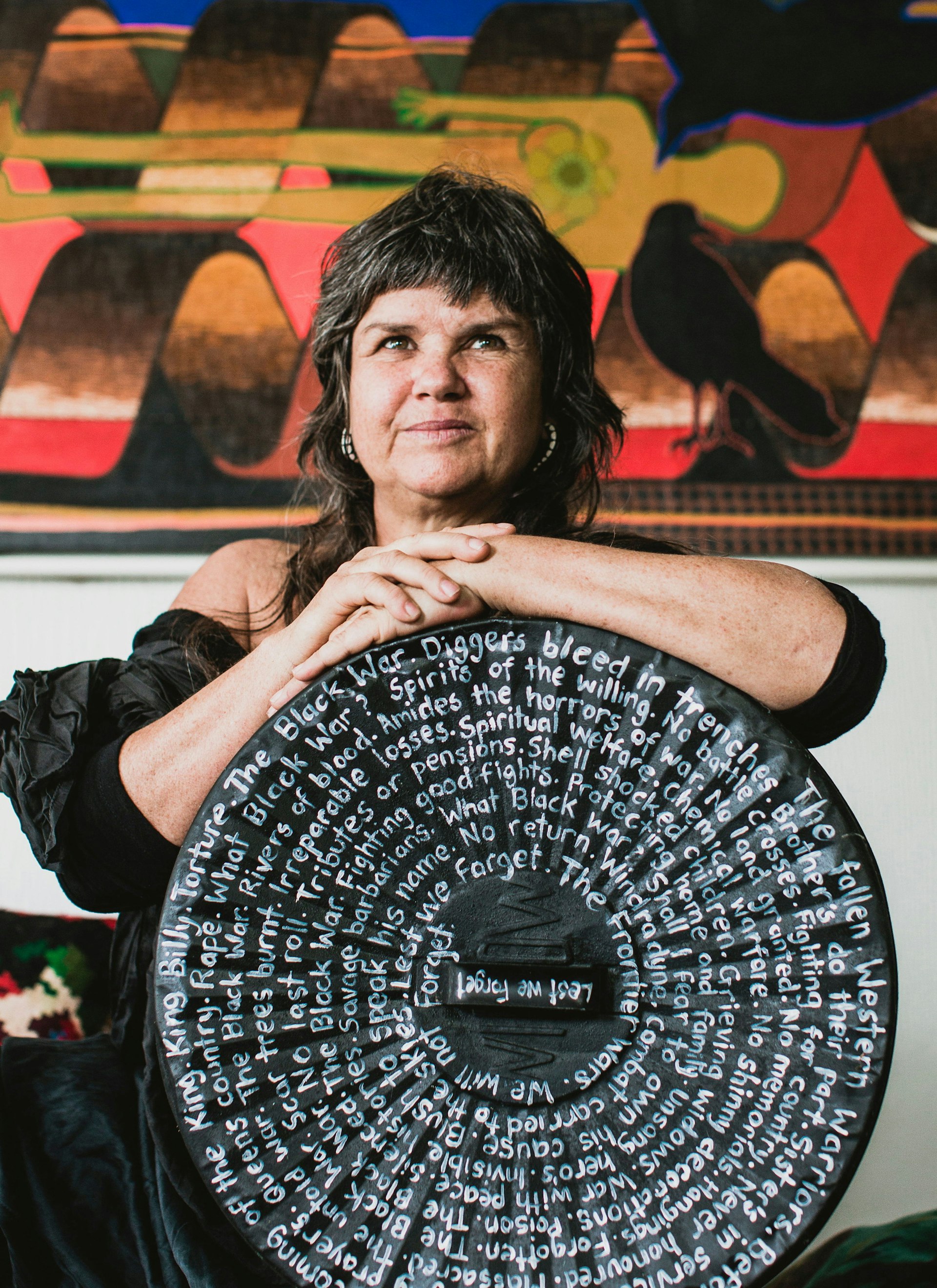 A woman stands holding a round black piece of art with writing on it. 
