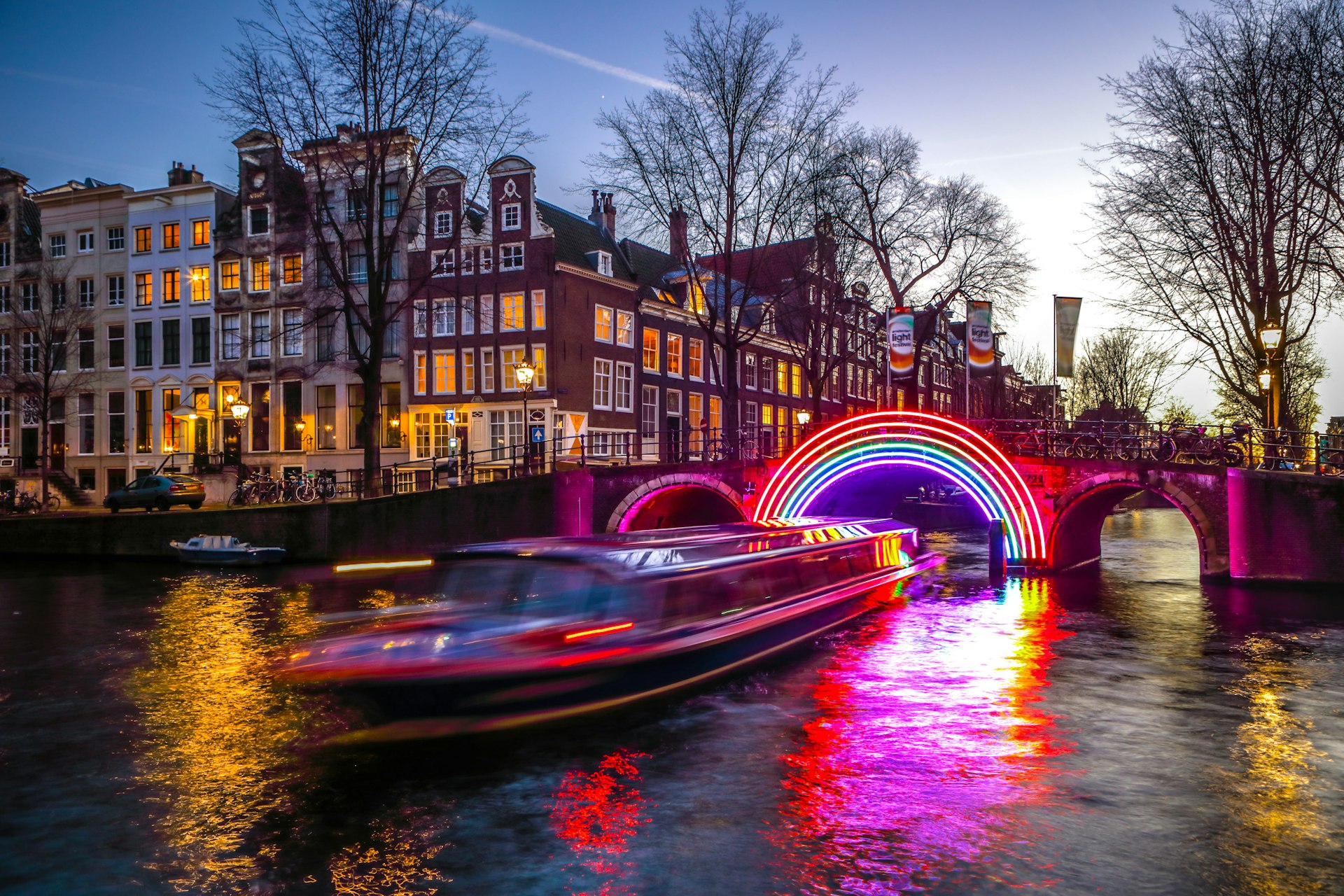 A boat passing through holiday light installations on an Amsterdam canal at night