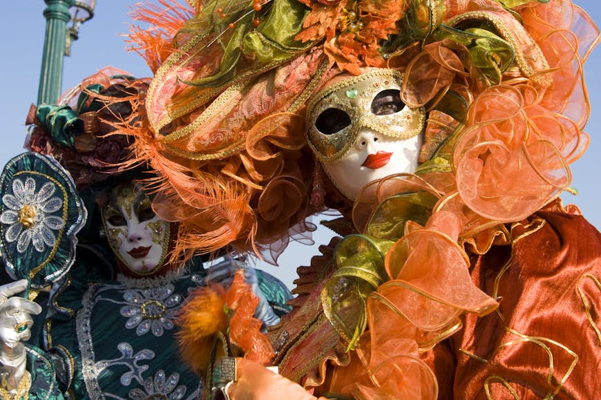 People in masks and Venetians costumes look into the camera. 