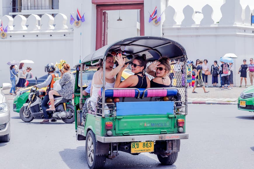 Three women smile and wave from the back of a three-wheeled vehicle 