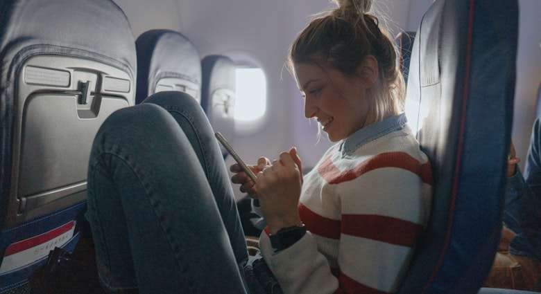 Photo of a young woman checking her smartphone during a flight.