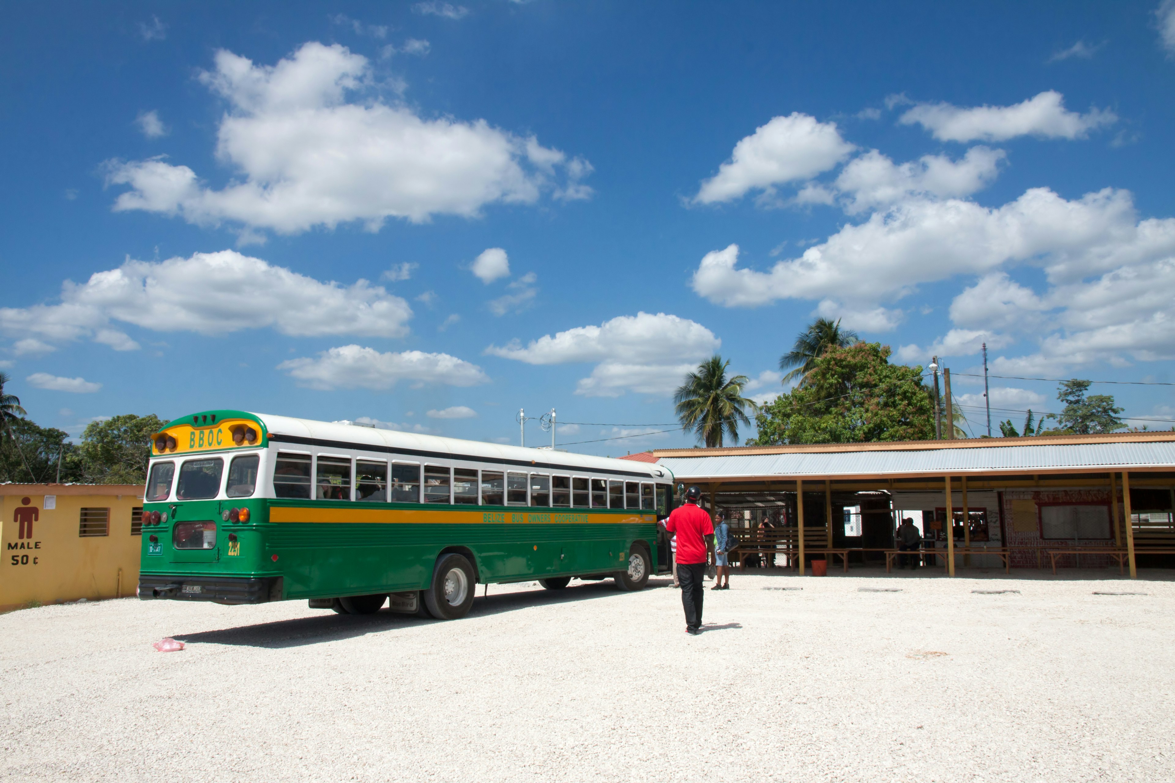 People walk to a cream and green bus stopped at the bus station near Belize City in a sunny day