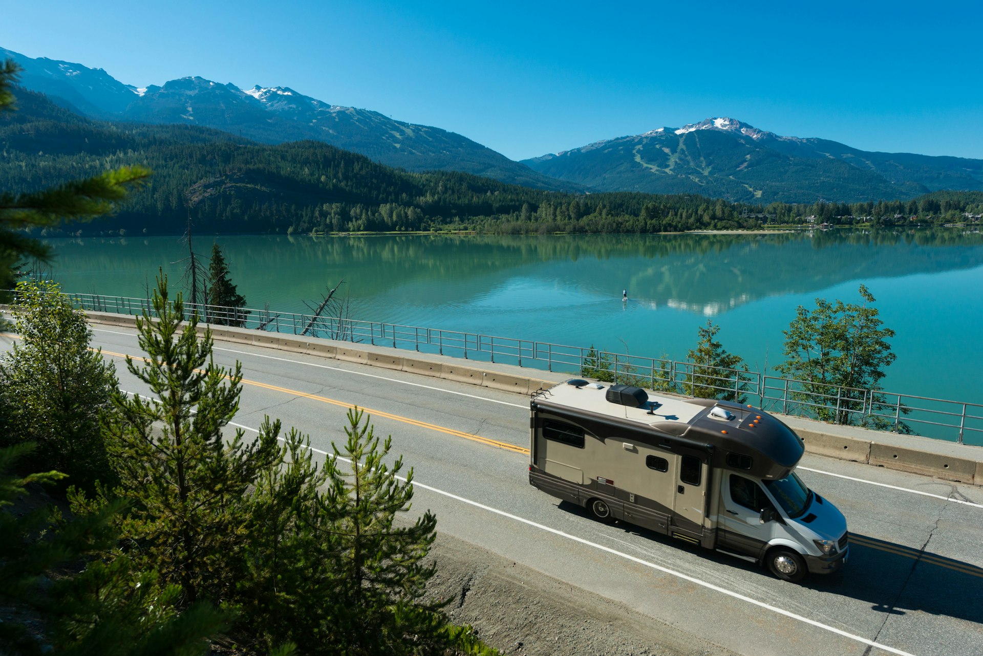 Large RV driving along a highway that hugs the edge of a turquoise lake