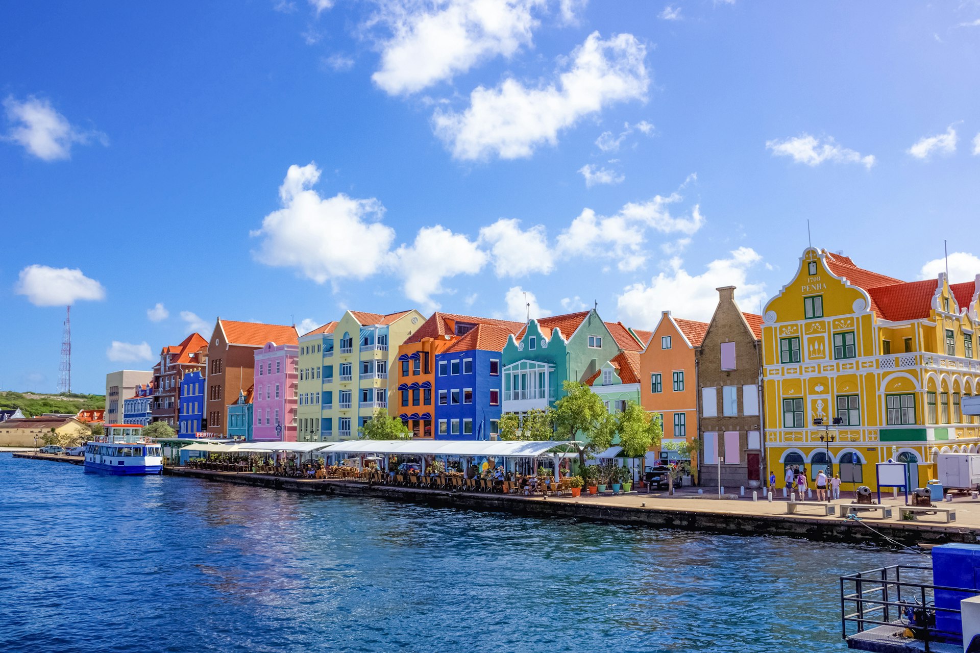 A row of pastel-colored buildings with outside tables line a harbor in Curacao