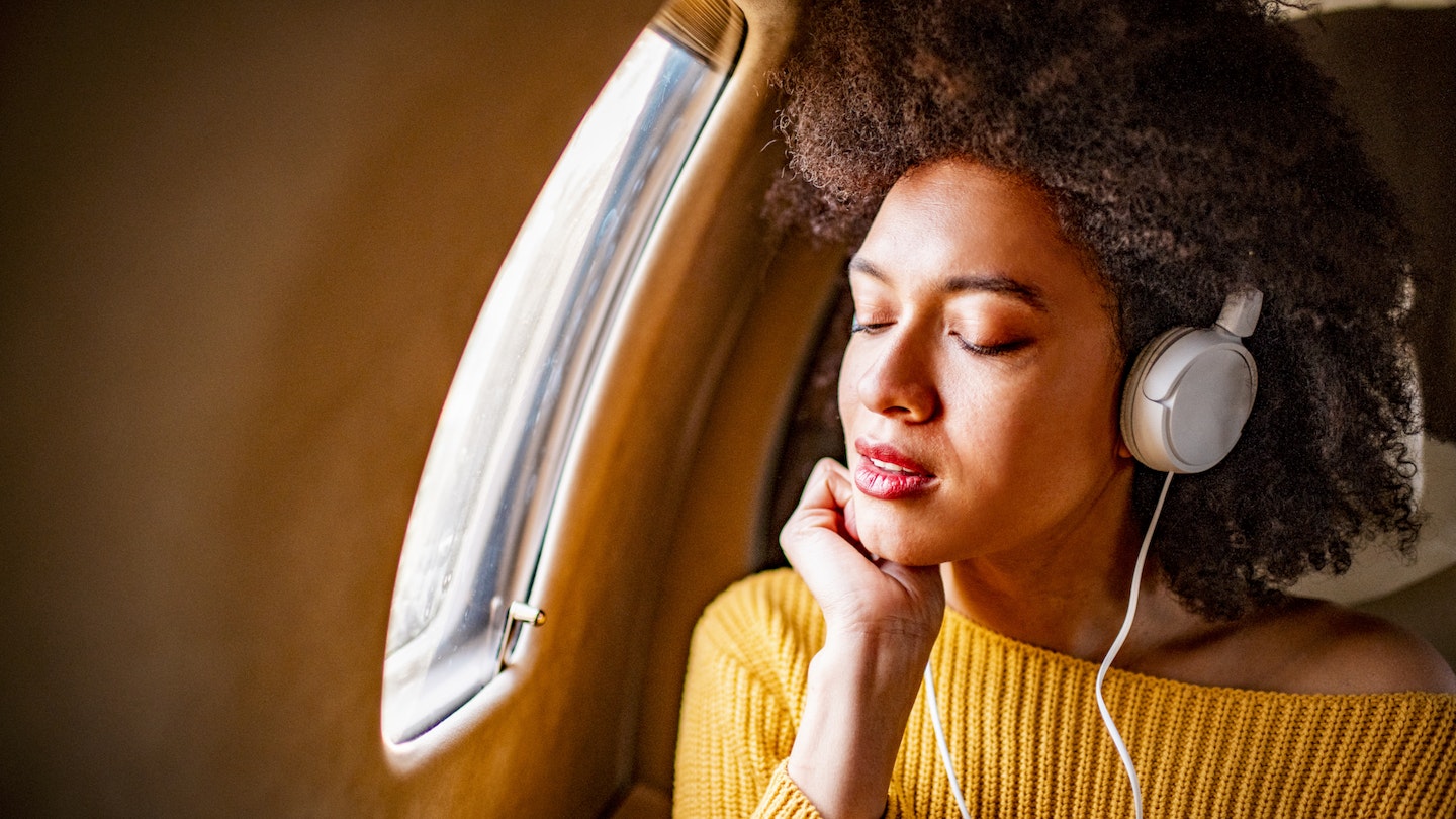 Young fashionable woman sitting on a private airplane with her eyes closed while listening to music through headphones.