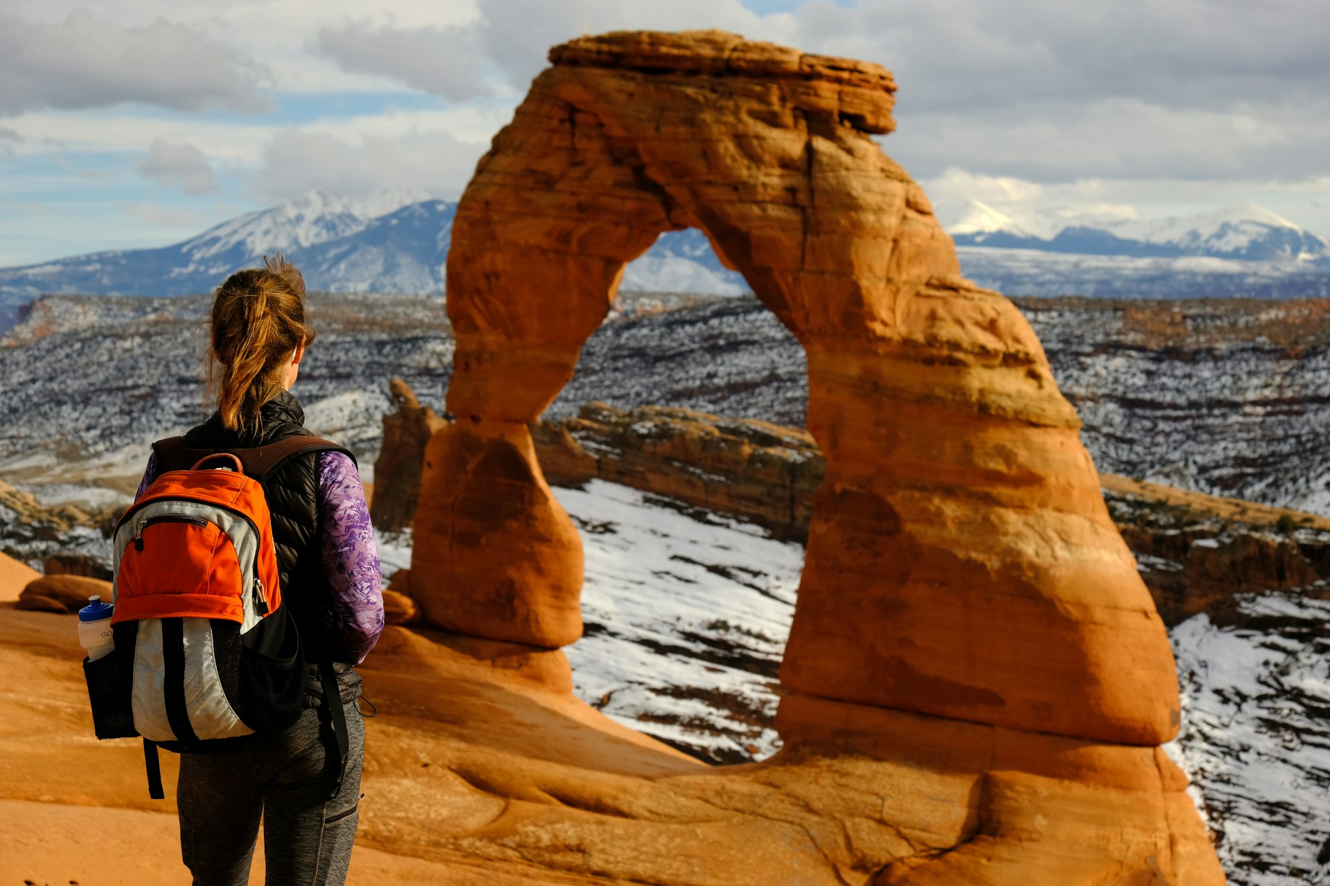 A woman hiker stands in front of a stone arch in a US national park. 