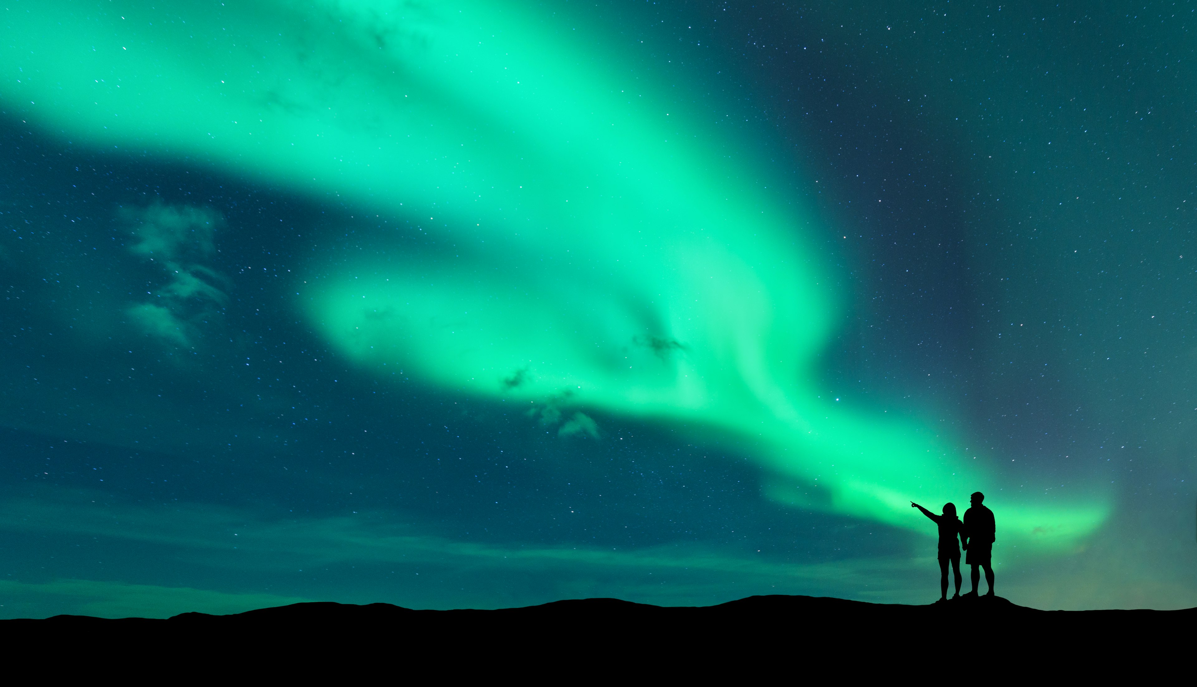 Aurora borealis and silhouette of standing man and woman who pointing finger on northern lights. Lofoten islands,Norway. Aurora. Sky with stars and polar lights.