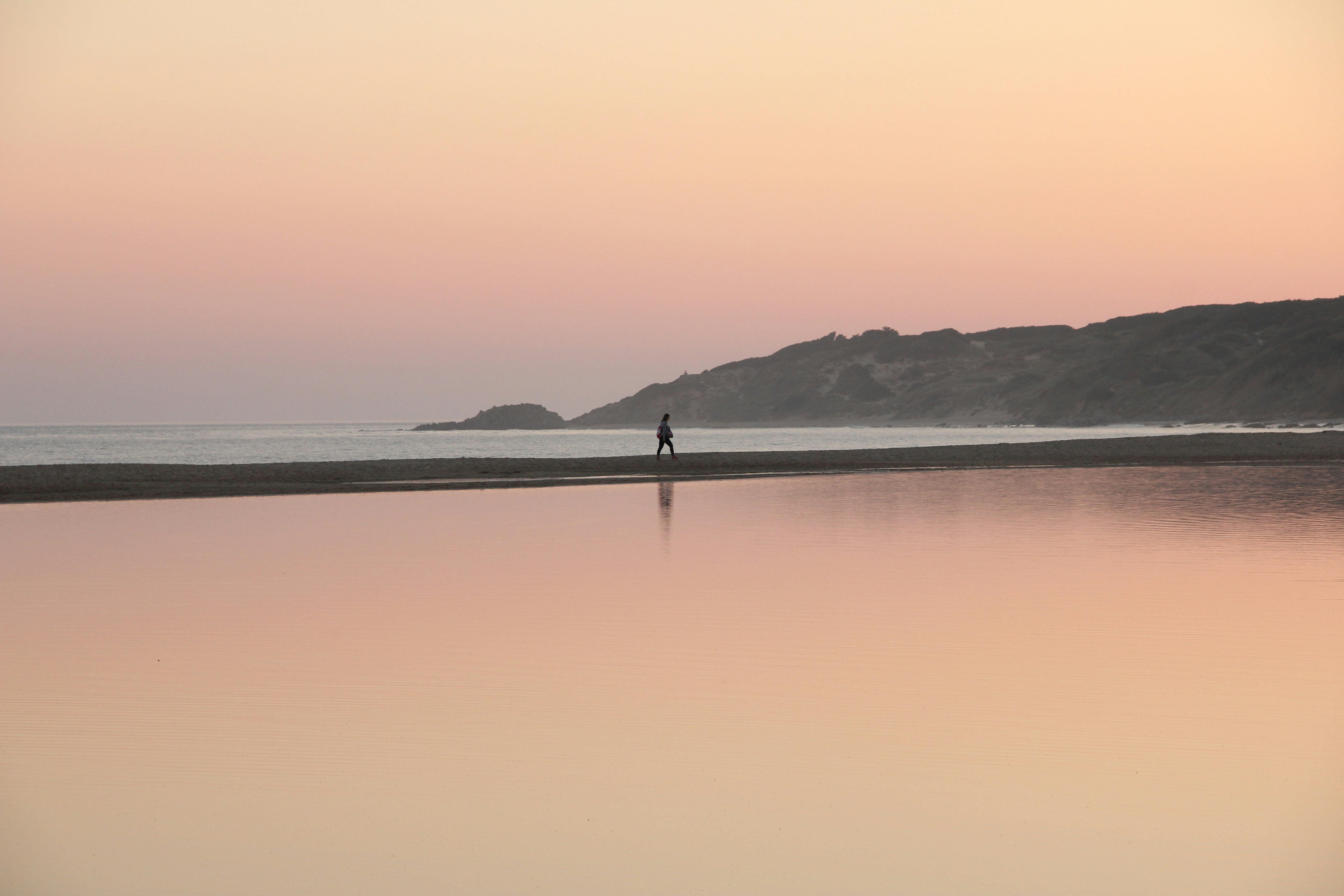 A woman walks along a sunset beach.