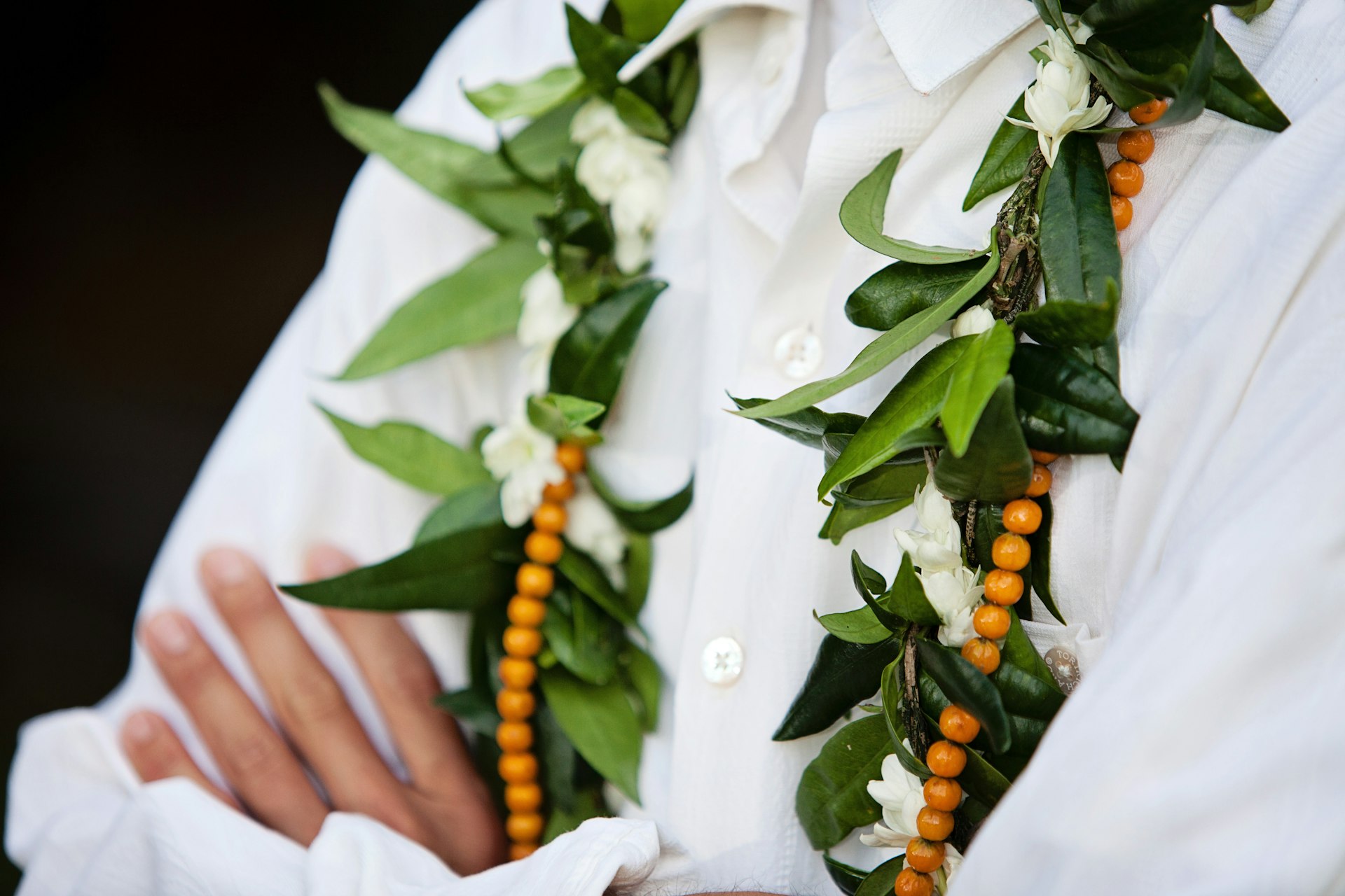 A garland of beads, white flowers and green leaves worn around someone's neck
