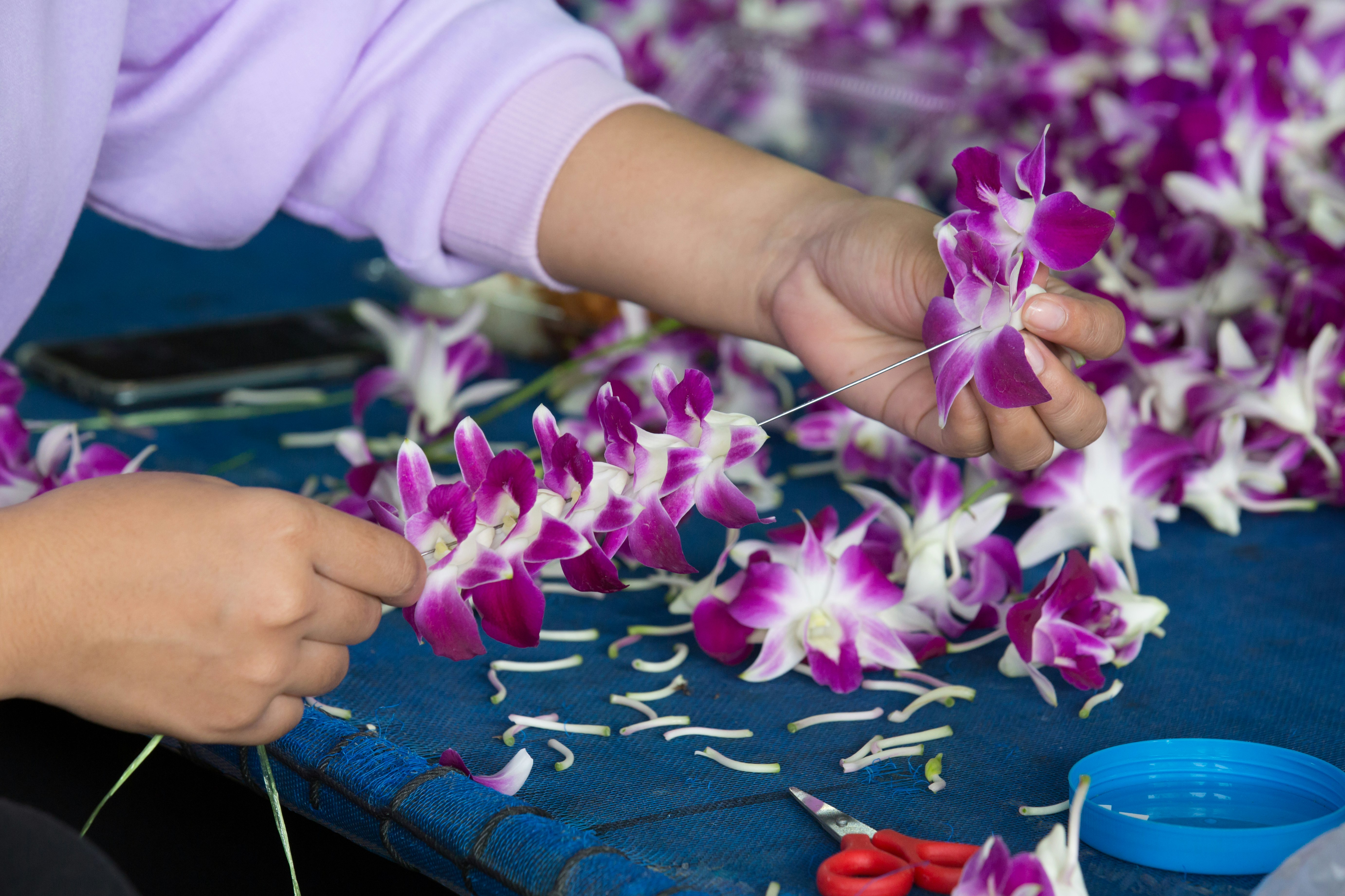 Hands thread petals onto string, forming a lei