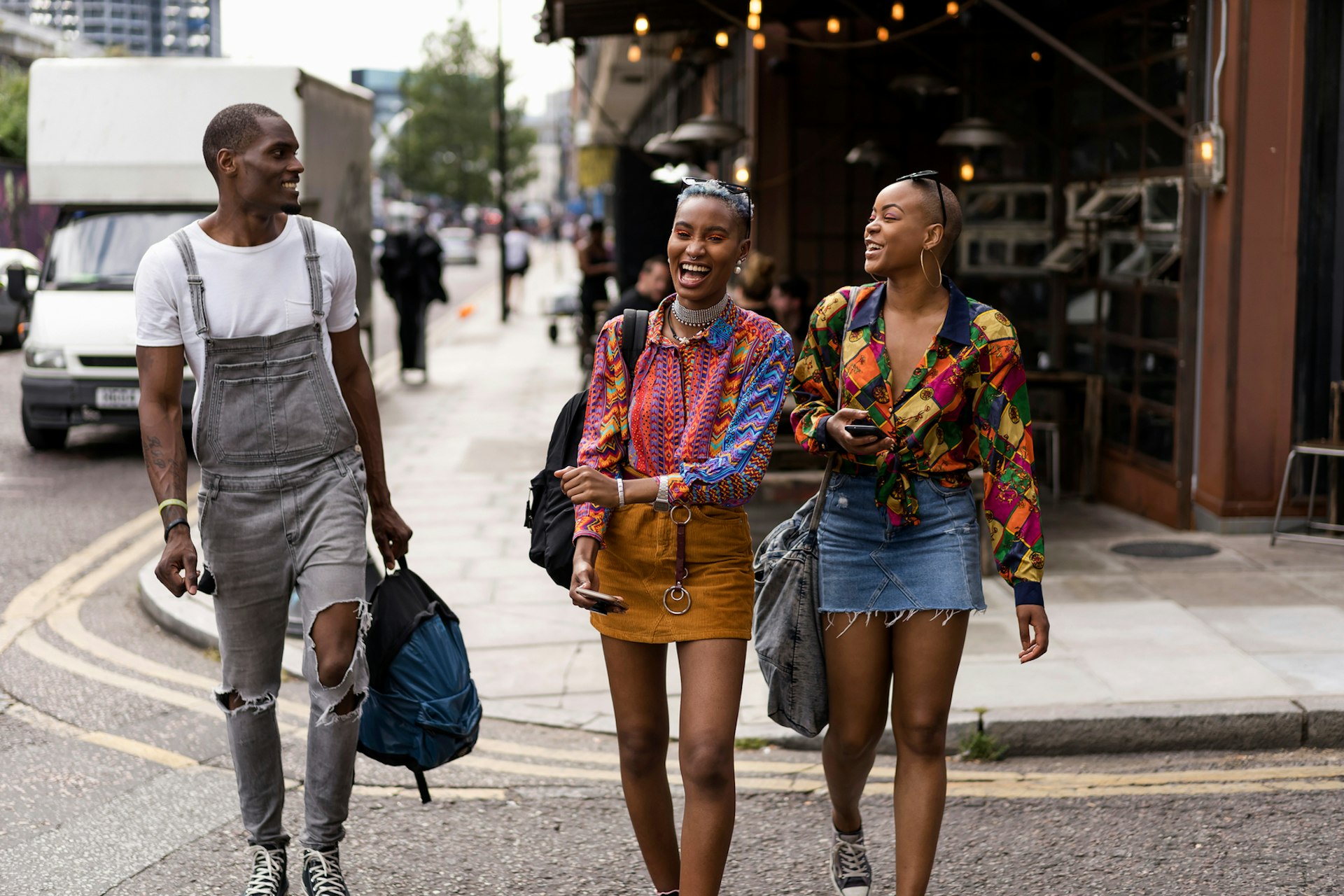 Two women and one man walk along a London street together while smiling and laughing