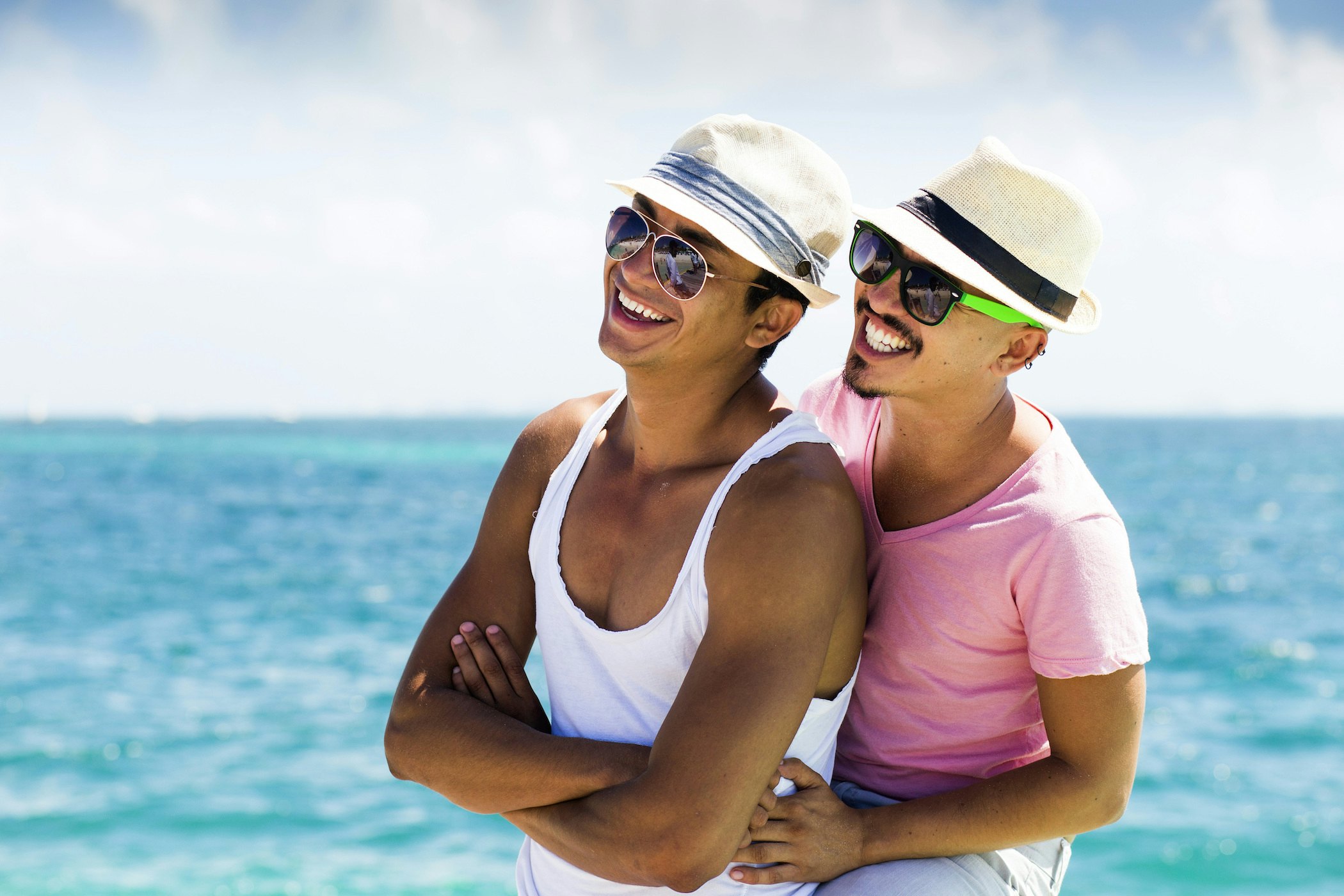 A male couple in hats smiles by the waters off Isla Mujeres, Quintana Roo, Mexico