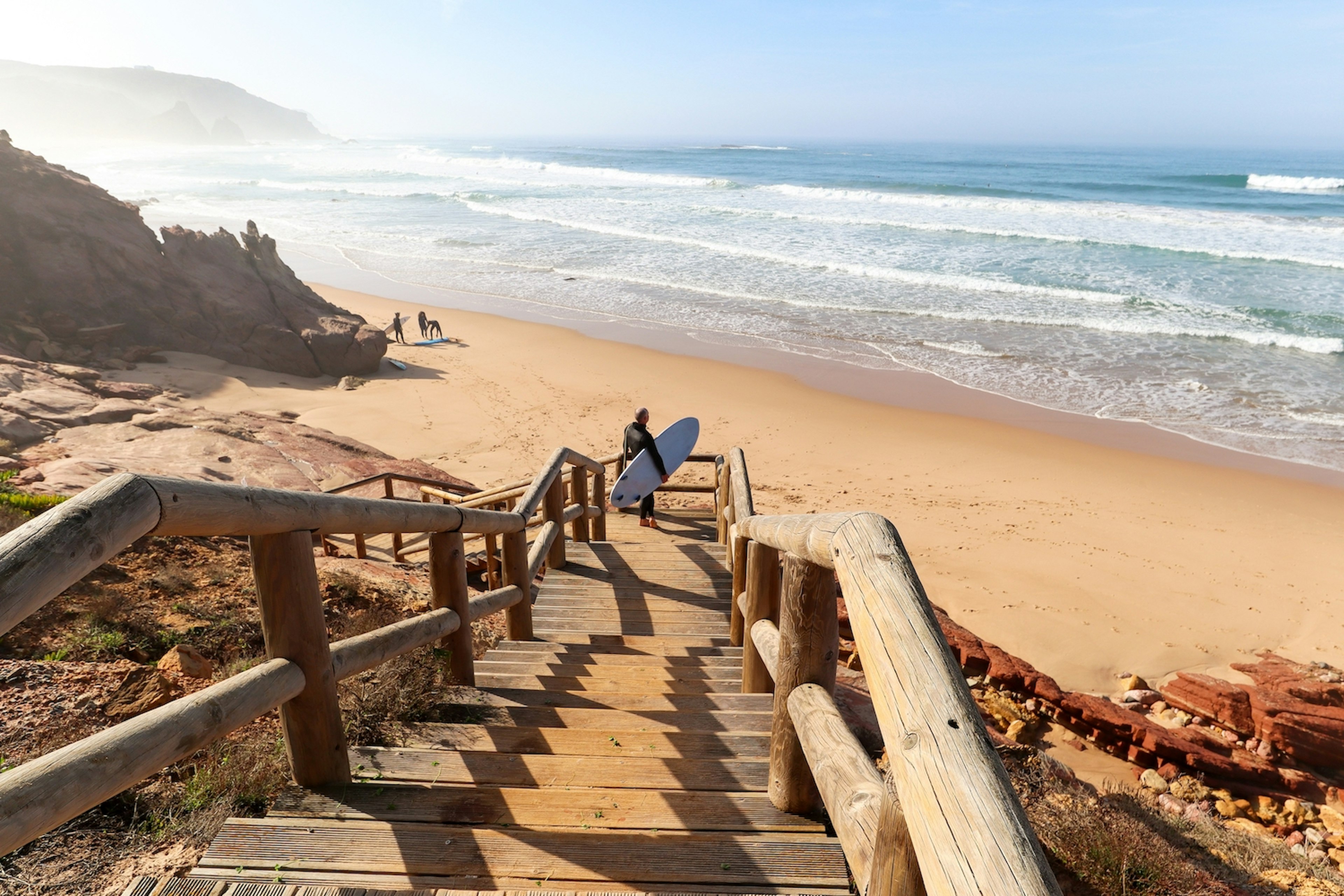 A surfer descends a wooden staircase to Praia do Amado, near Sagres, Costa Vicentina, the Algarve Portugal