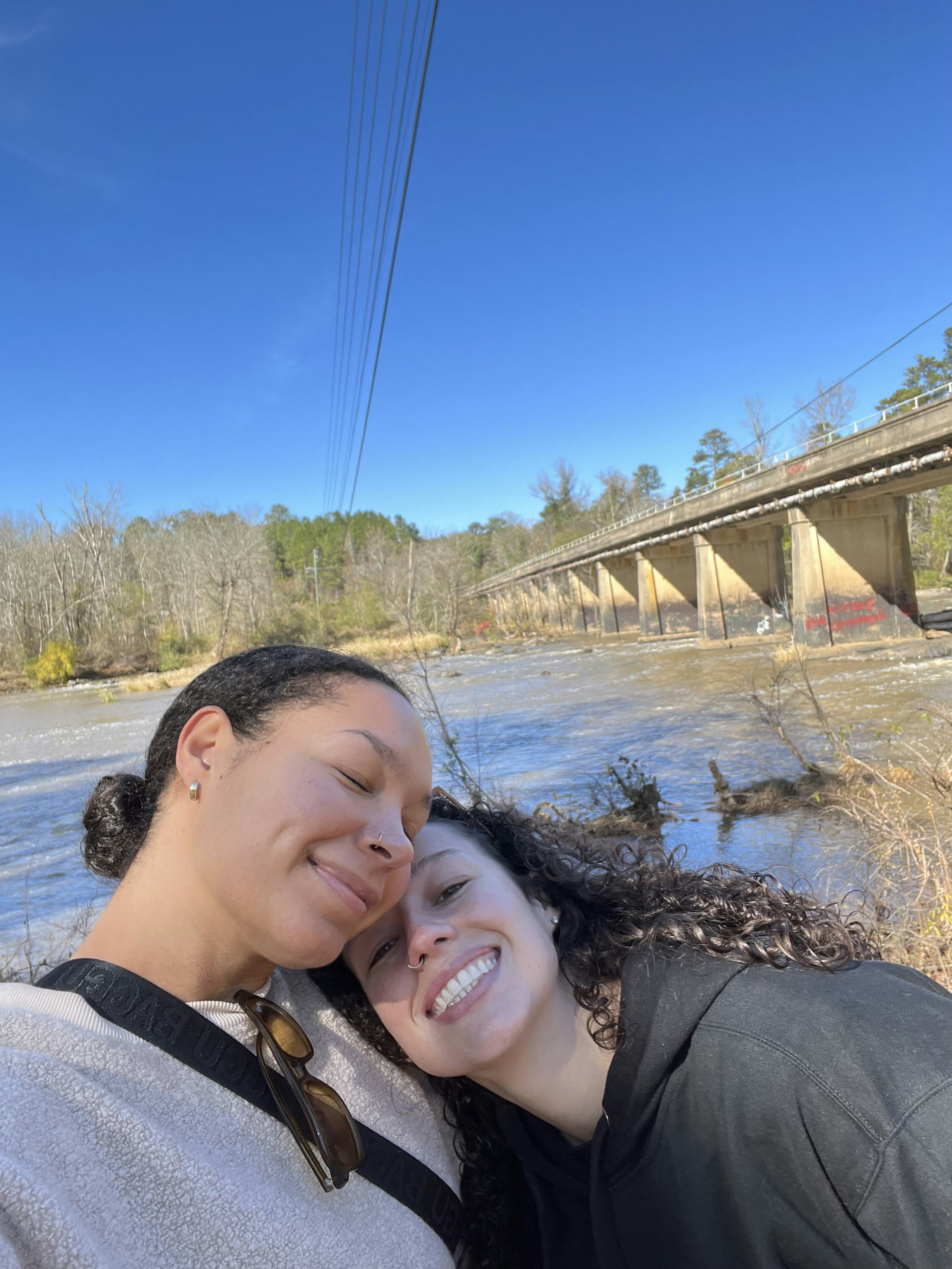 Two women cuddle on the banks of the river.