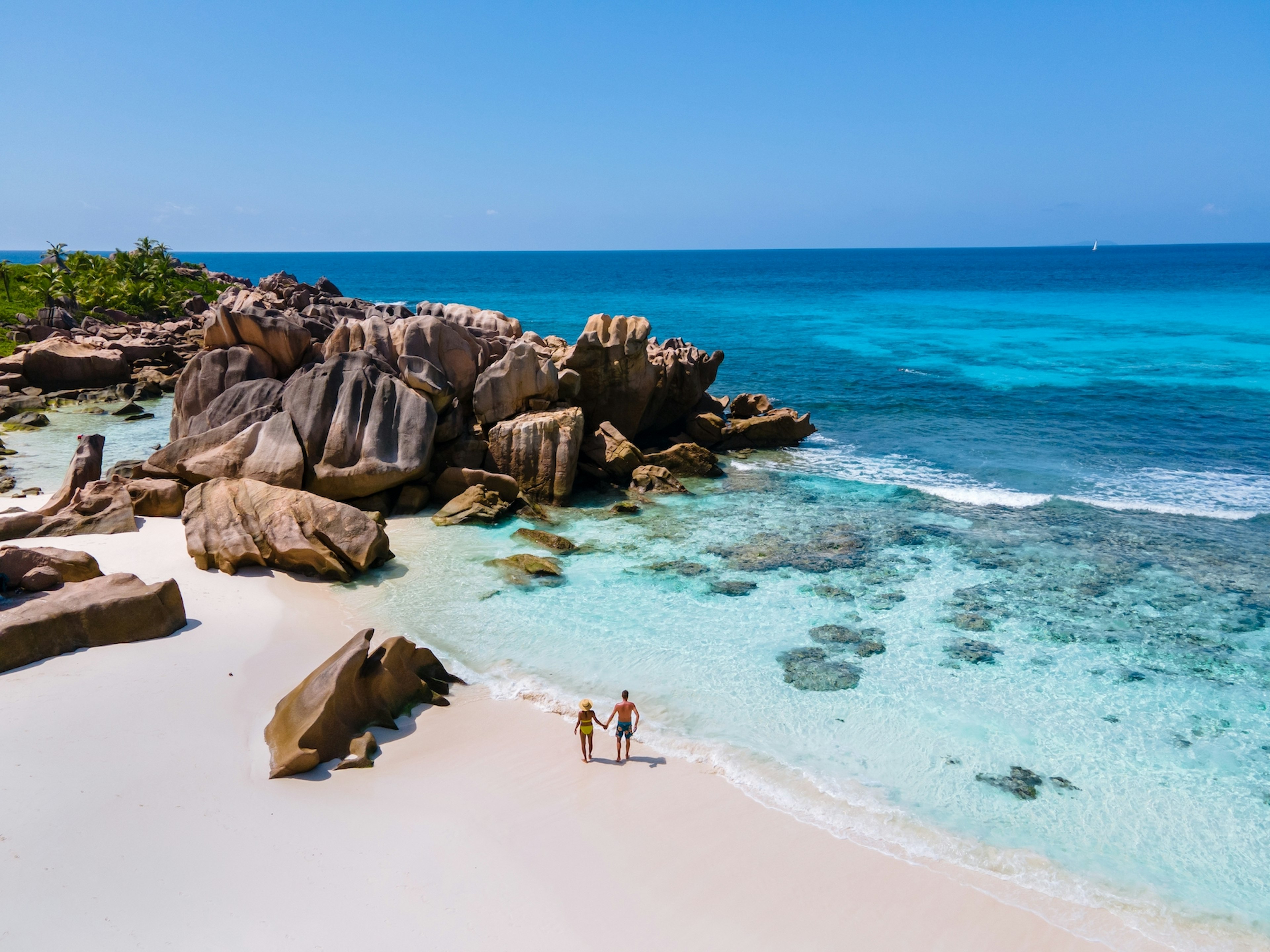 An aerial view of a man and woman waking on the boulder-strewn beach of Anse Cocos, La Digue, Seychelles