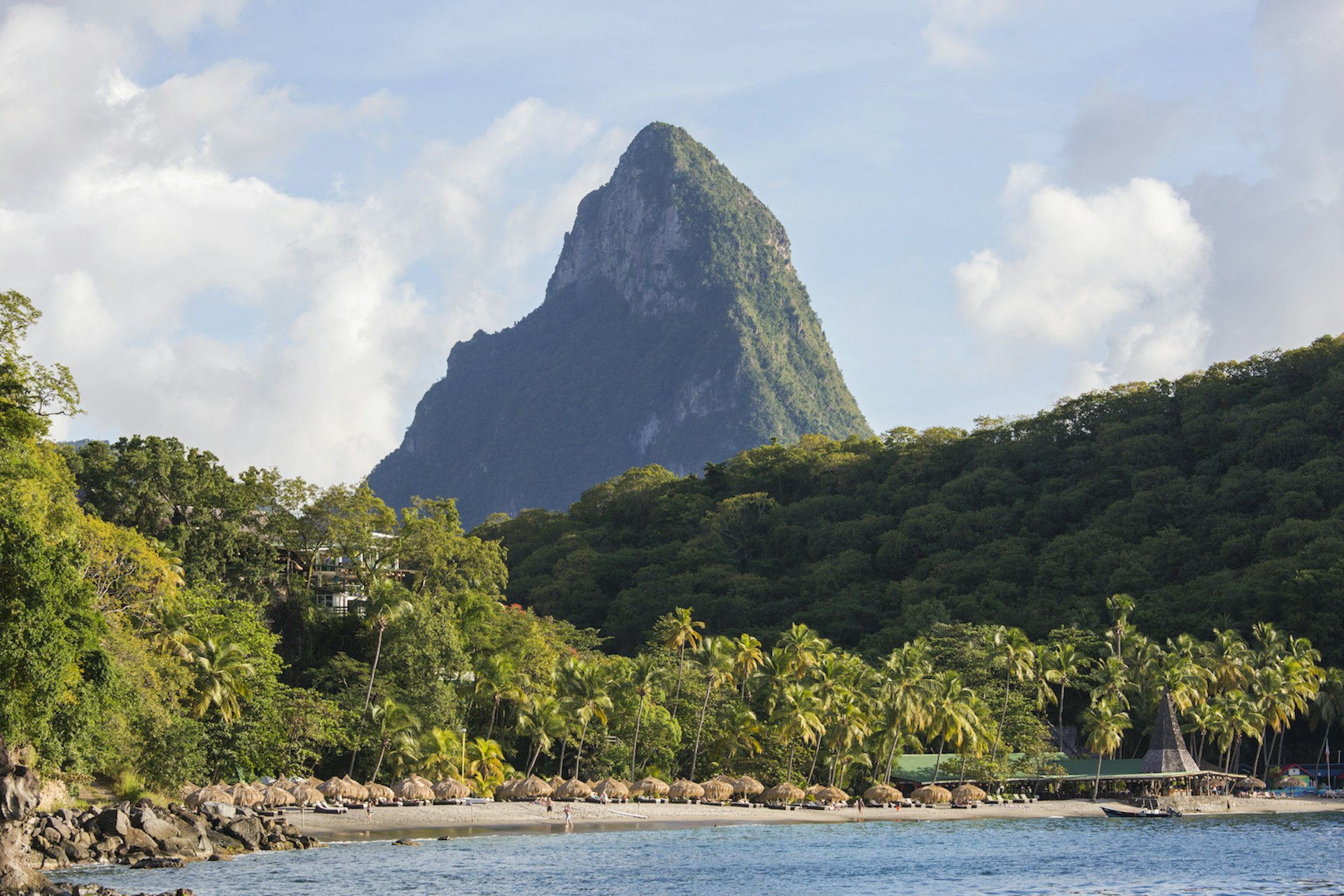 View across water to the palm-fringed beach of Anse Chastanet and steep rugged slopes of Petit Piton, evening, Soufrière, St Lucia, West Indies, North America