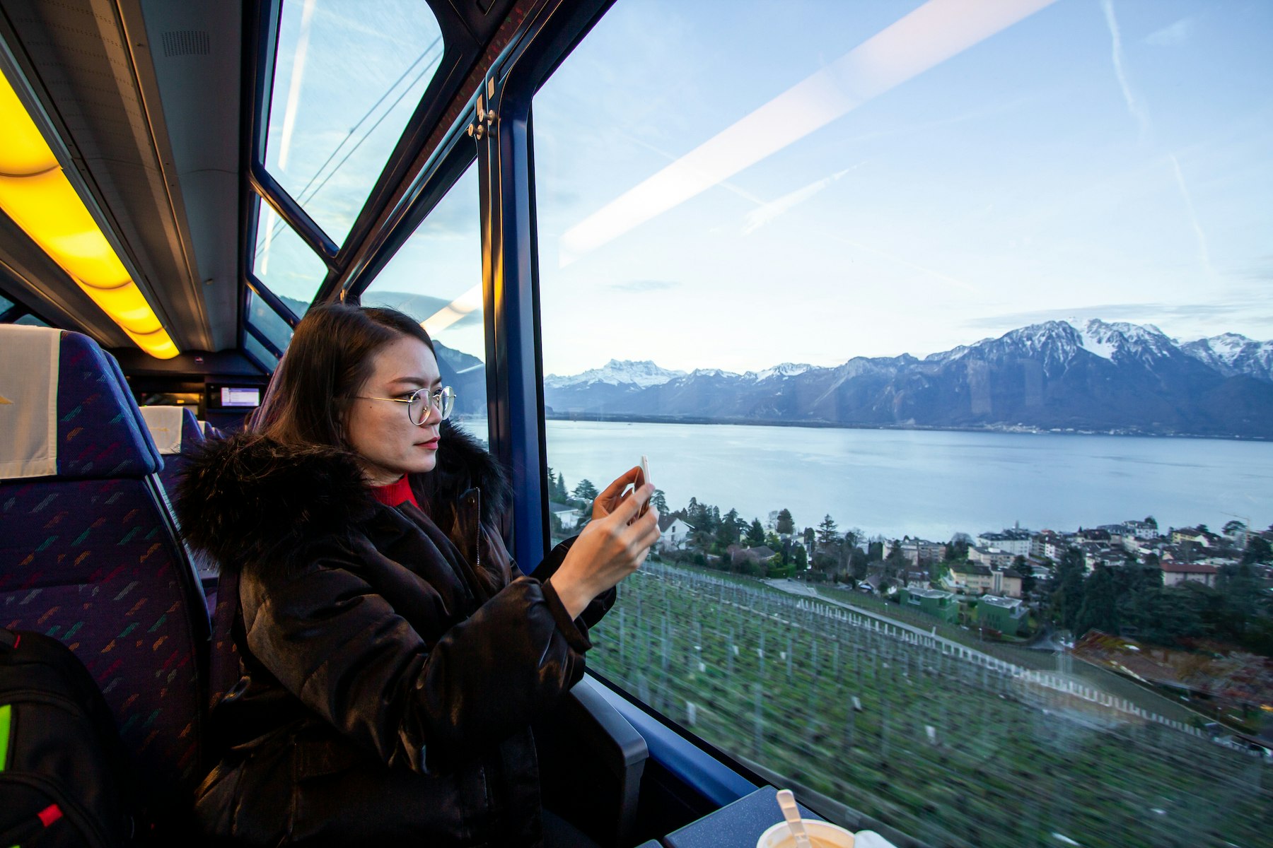 A woman takes a photo in the viewing car of the GoldenPass Express train between Montreux and Interlaken Ost, Switzerland