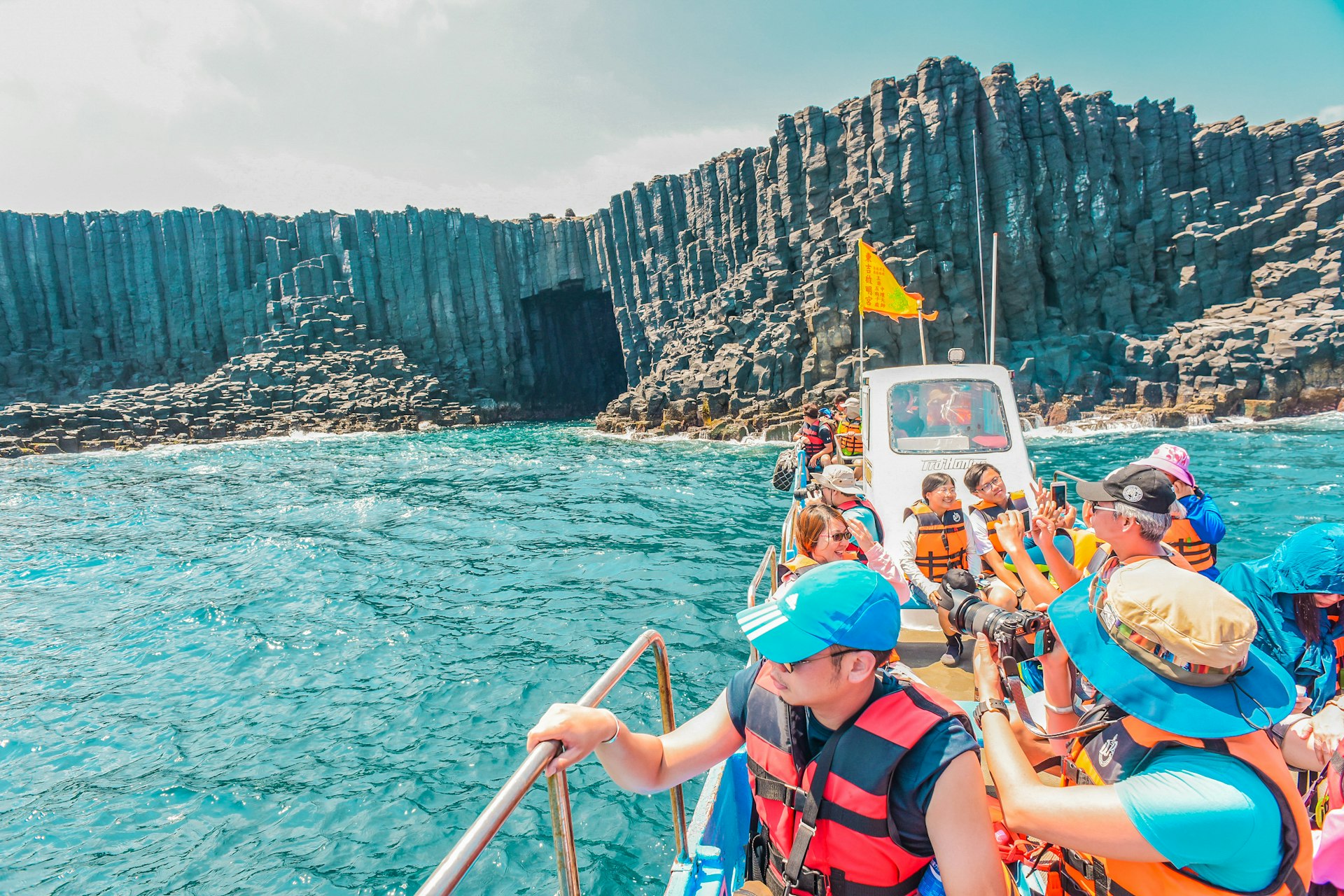 A boat loaded with tourists explores the natural stone features that line an island coastline