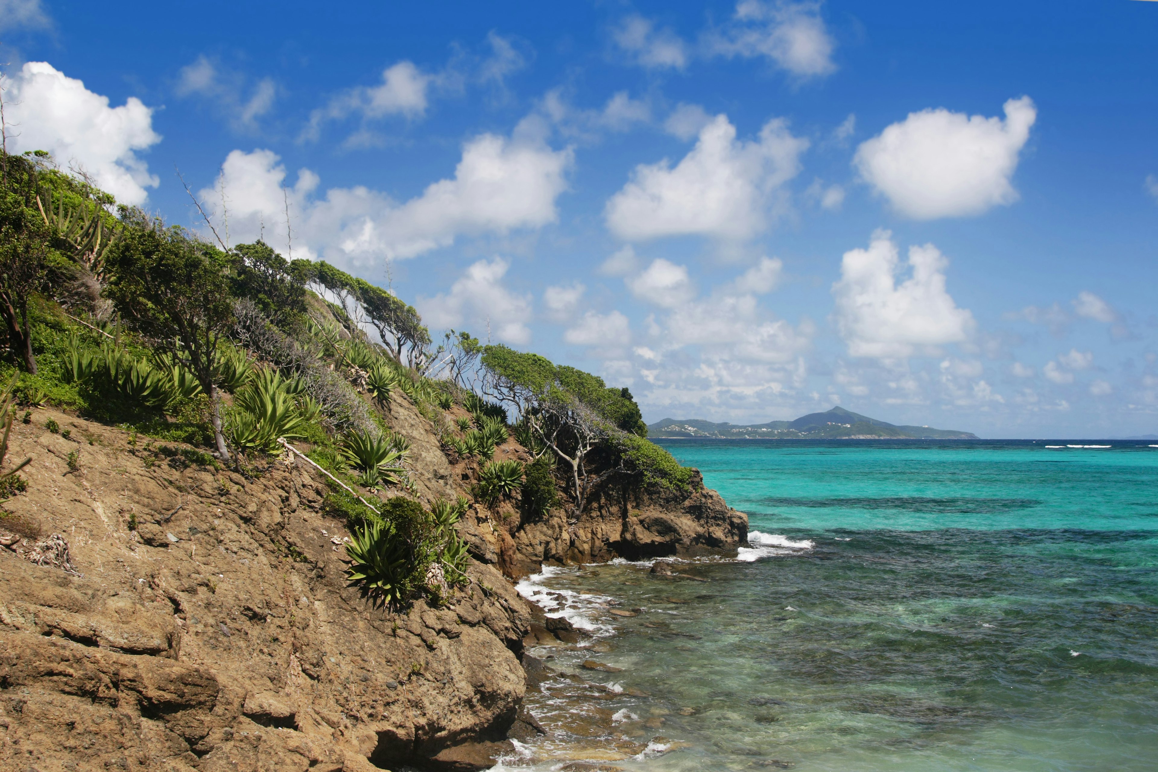 An island drops down into a turquoise ocean with more islands in the distance across the water