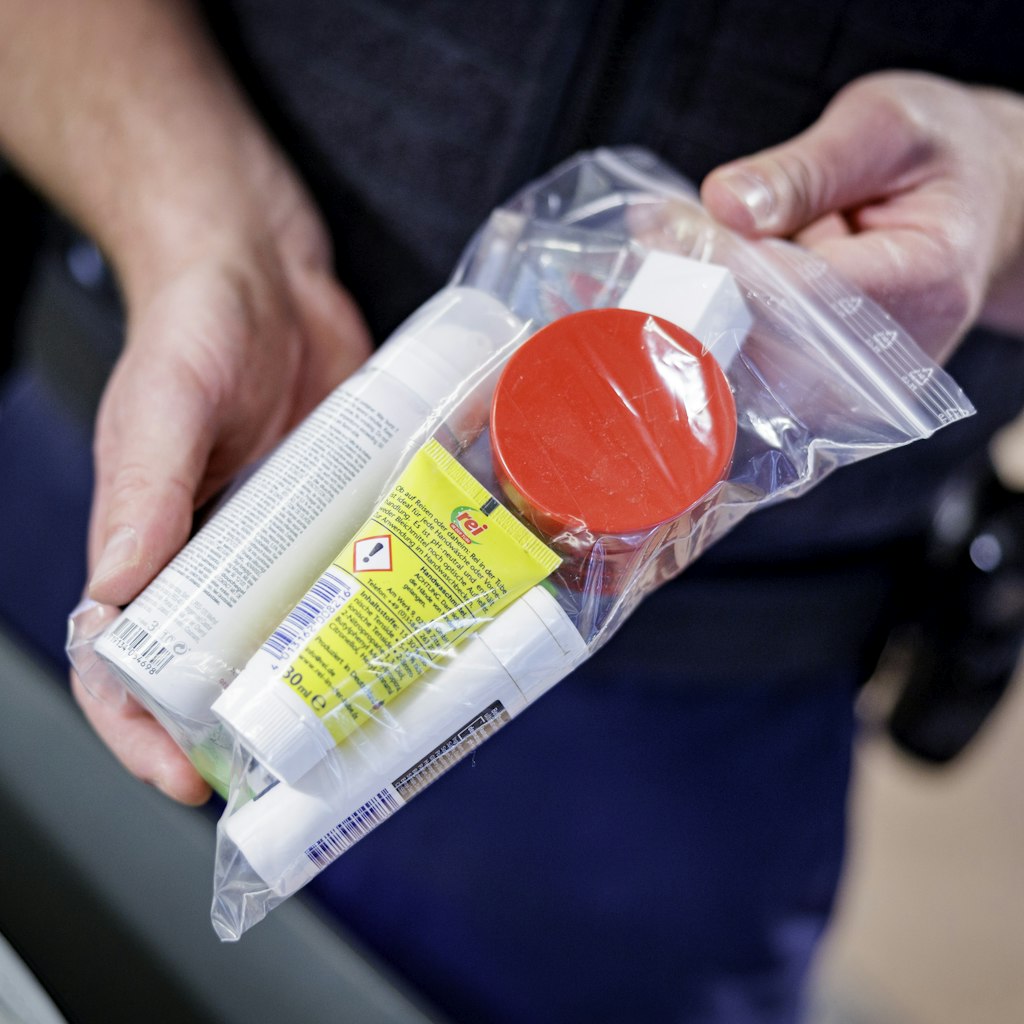 22 June 2022, Hamburg: An officer of the Federal Police shows at Hamburg Airport during the security check which quantities of liquids may be carried and how they must be packed.      (to dpa "Busy at the airport - this is how the security check works") P