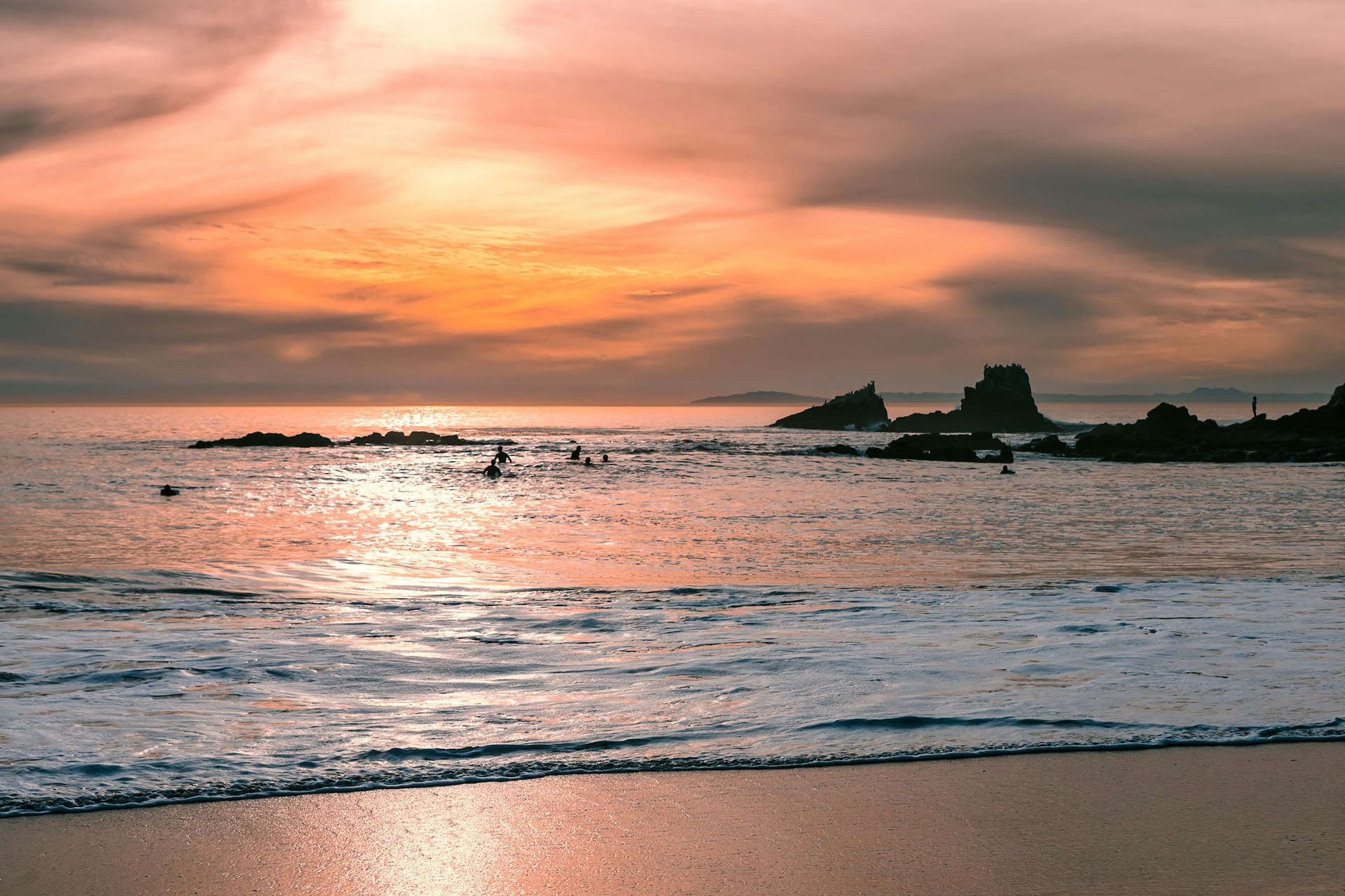 A small group of surfers on their boards in the water waiting for waves during sunset at Crescent Bay in Laguna Beach, CA