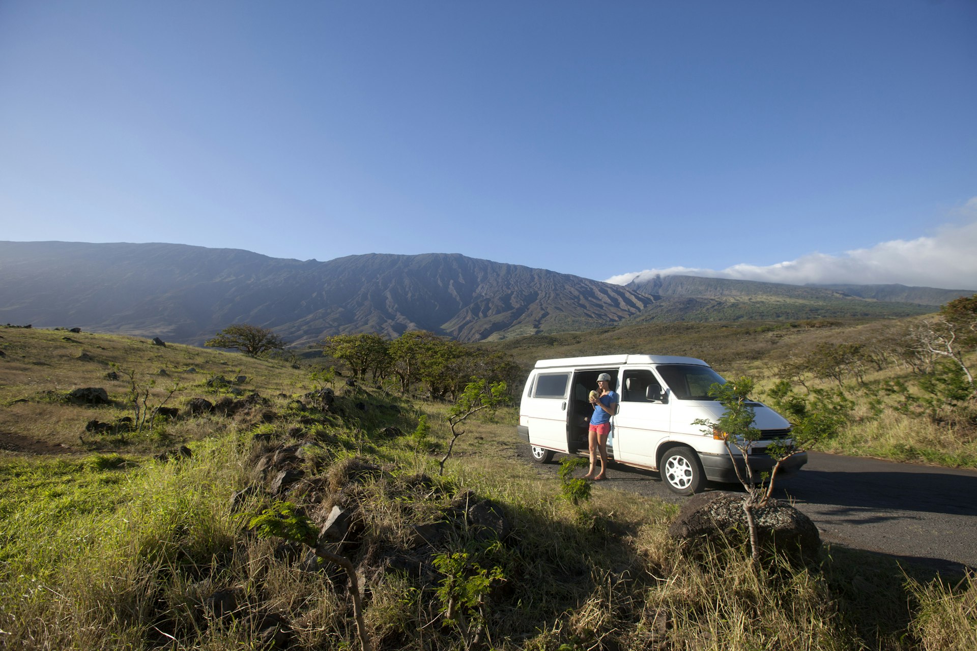 A woman leans on a camper van as she soaks up the view of hills rising around her