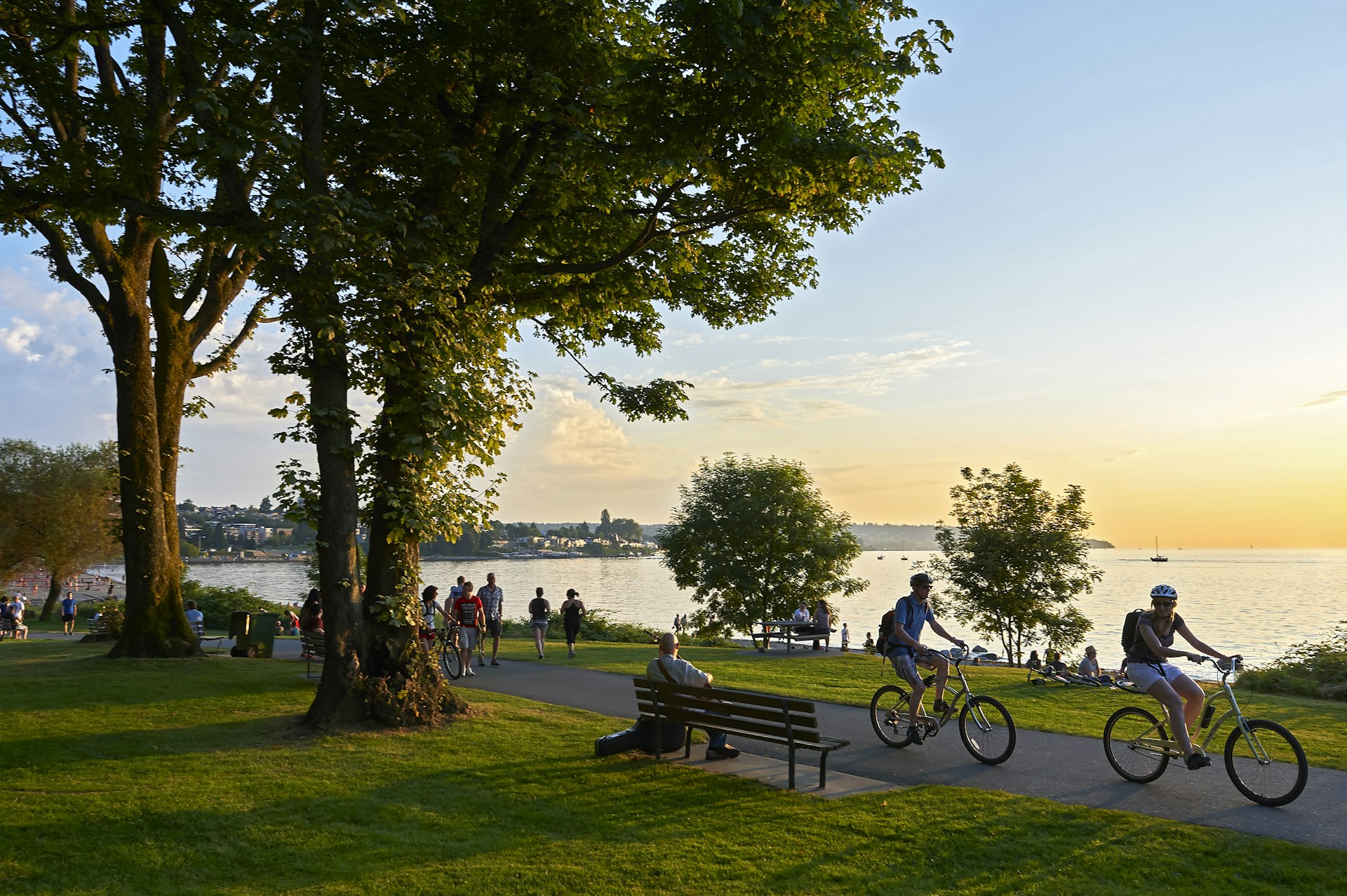 Young couple cycling, others walking or jogging in the late afternoon in a park by the sea