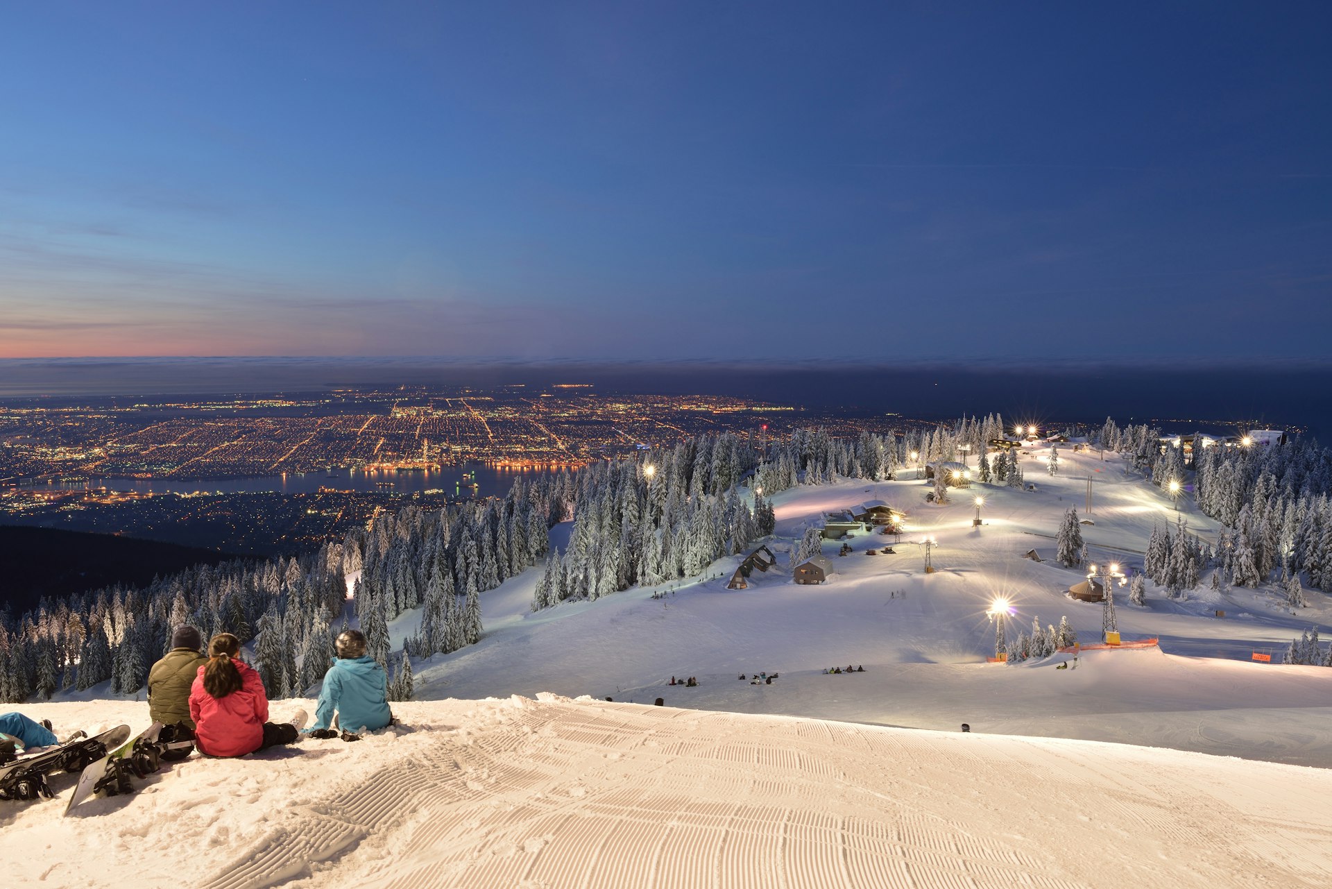 Three people - skiere and snowboarders - wait for sunrise on Grouse Mountain