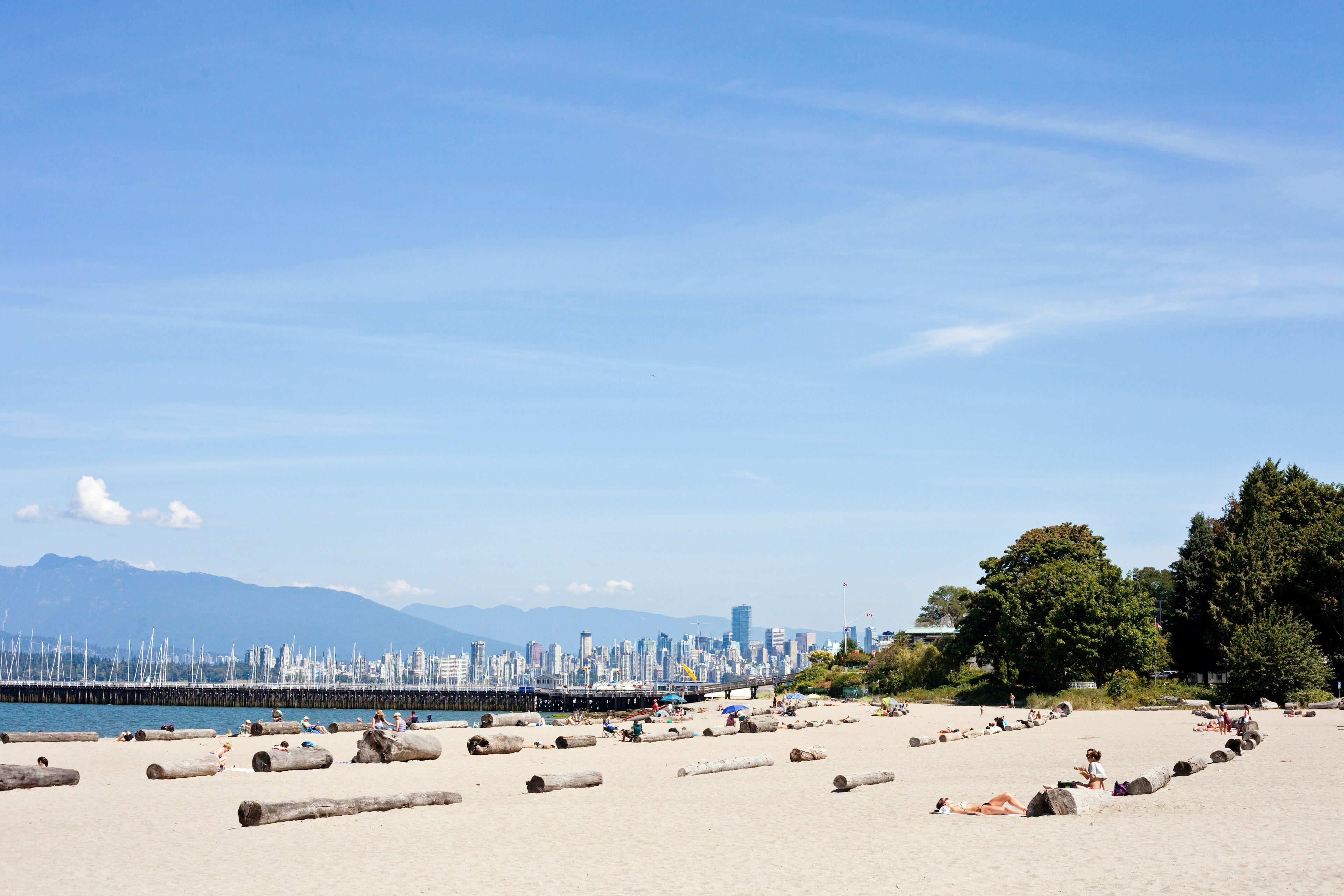 A summer day on Jericho Beach in Kitsilano. People are spread out on the beach with the city of Vancouver in the background