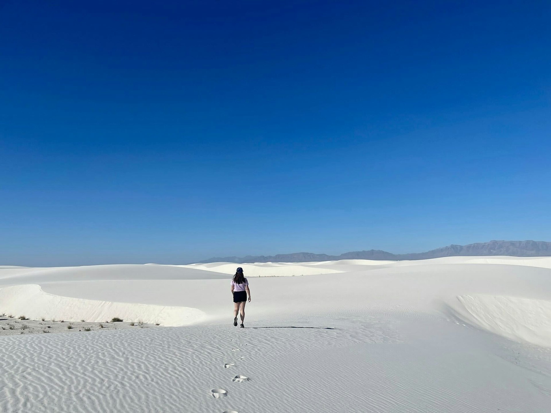 A woman walks through the white sand dunes of a national park. 