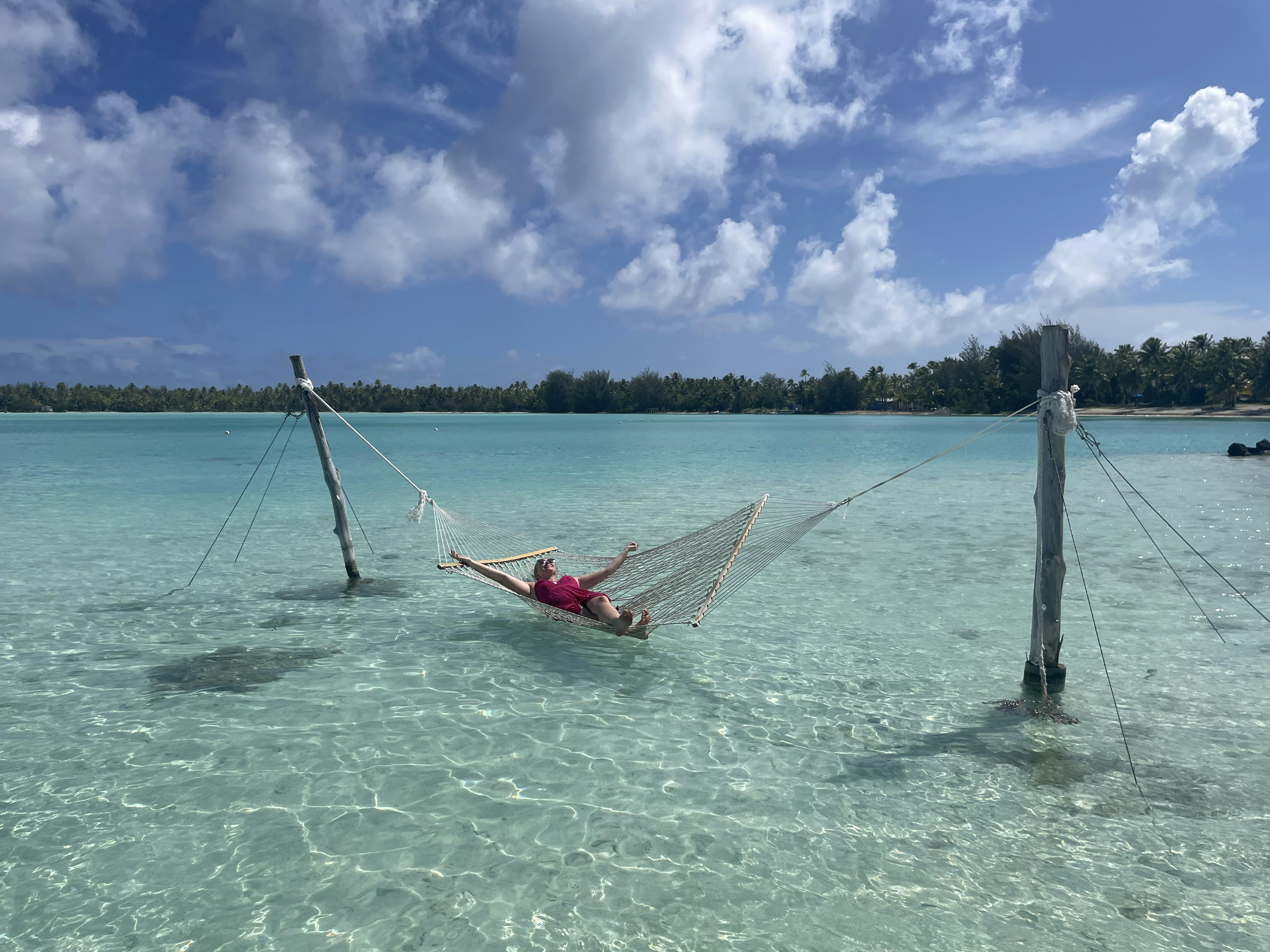 A woman lies on a hammock over blue water in Bora Bora.